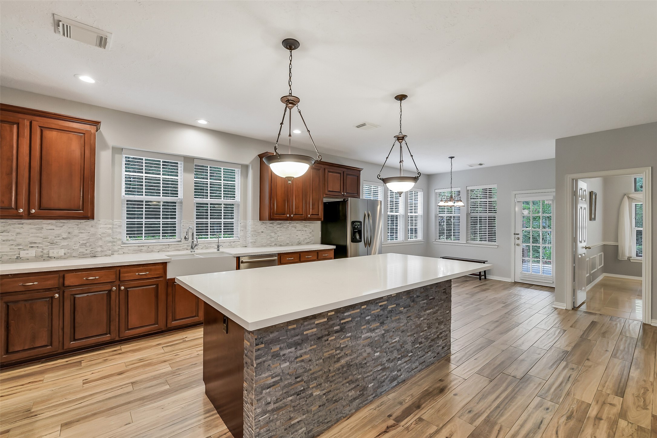 Spacious kitchen with elegant wood cabinetry, a large center island with stone accents, and modern stainless steel appliances. Natural light pours in through multiple windows, highlighting the sleek countertops and open layout.