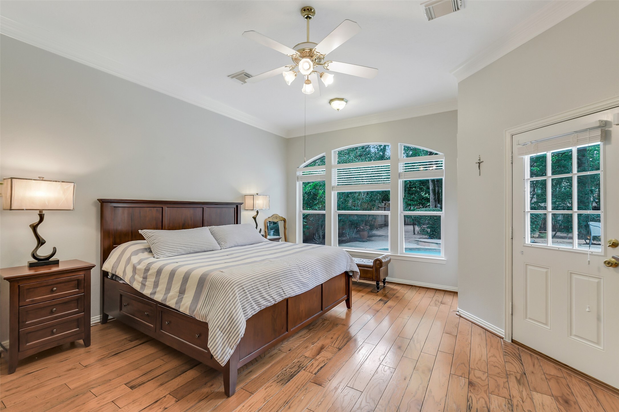 Spacious Primary bedroom with natural light, featuring elegant wood flooring, and a view of the lush backyard through large windows.