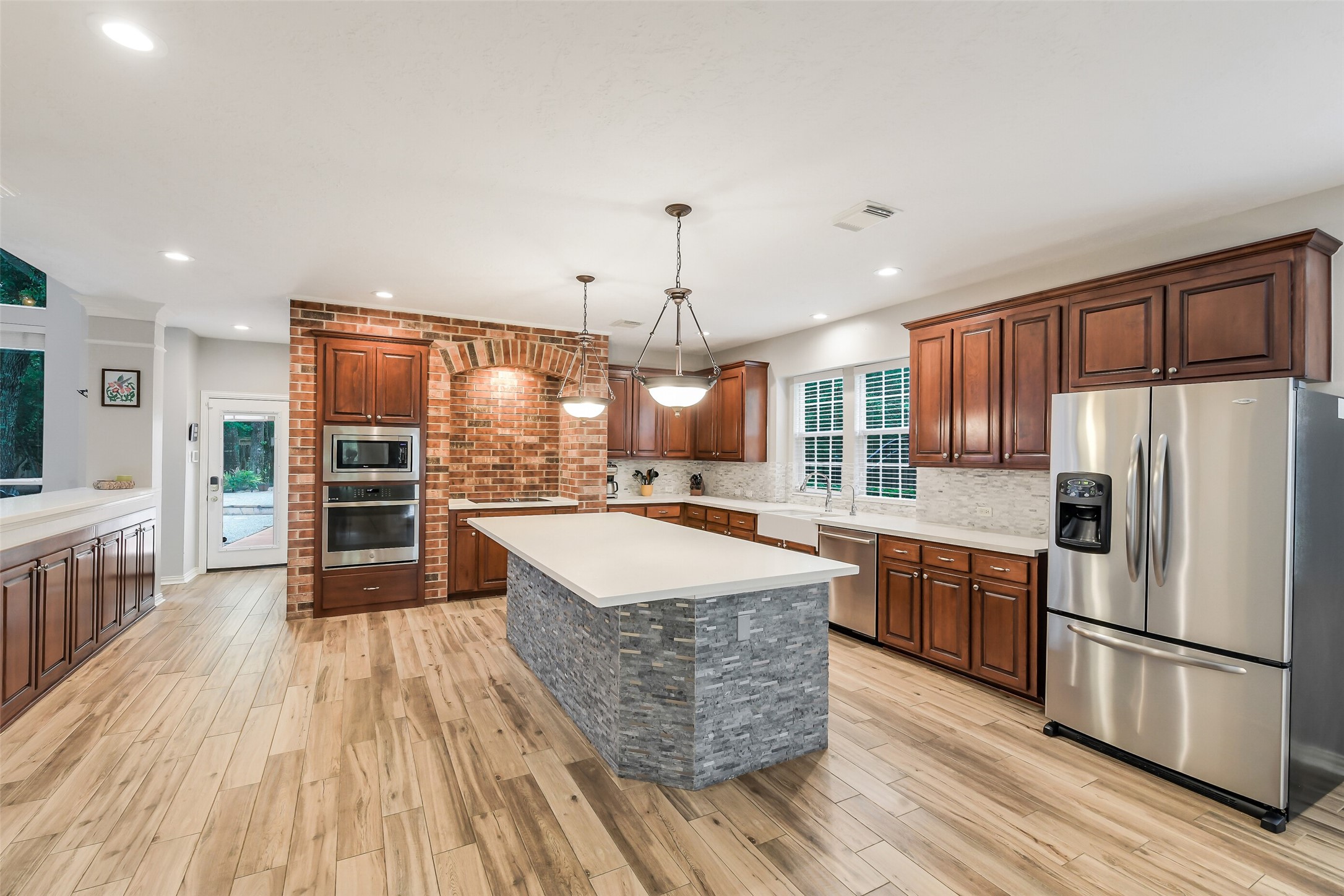 Spacious kitchen with elegant wooden cabinetry, a large central island with stone accents, stainless steel appliances, and a charming brick feature wall.