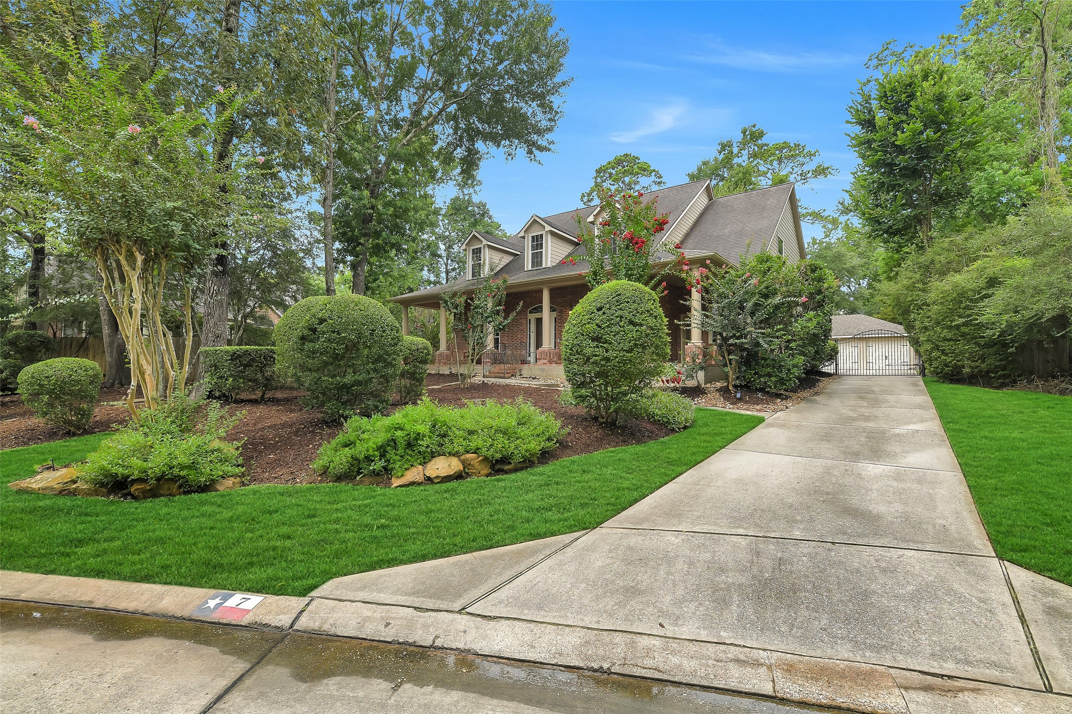 Charming home with a spacious front porch, surrounded by lush greenery and mature trees, featuring a long driveway leading to a detached garage.