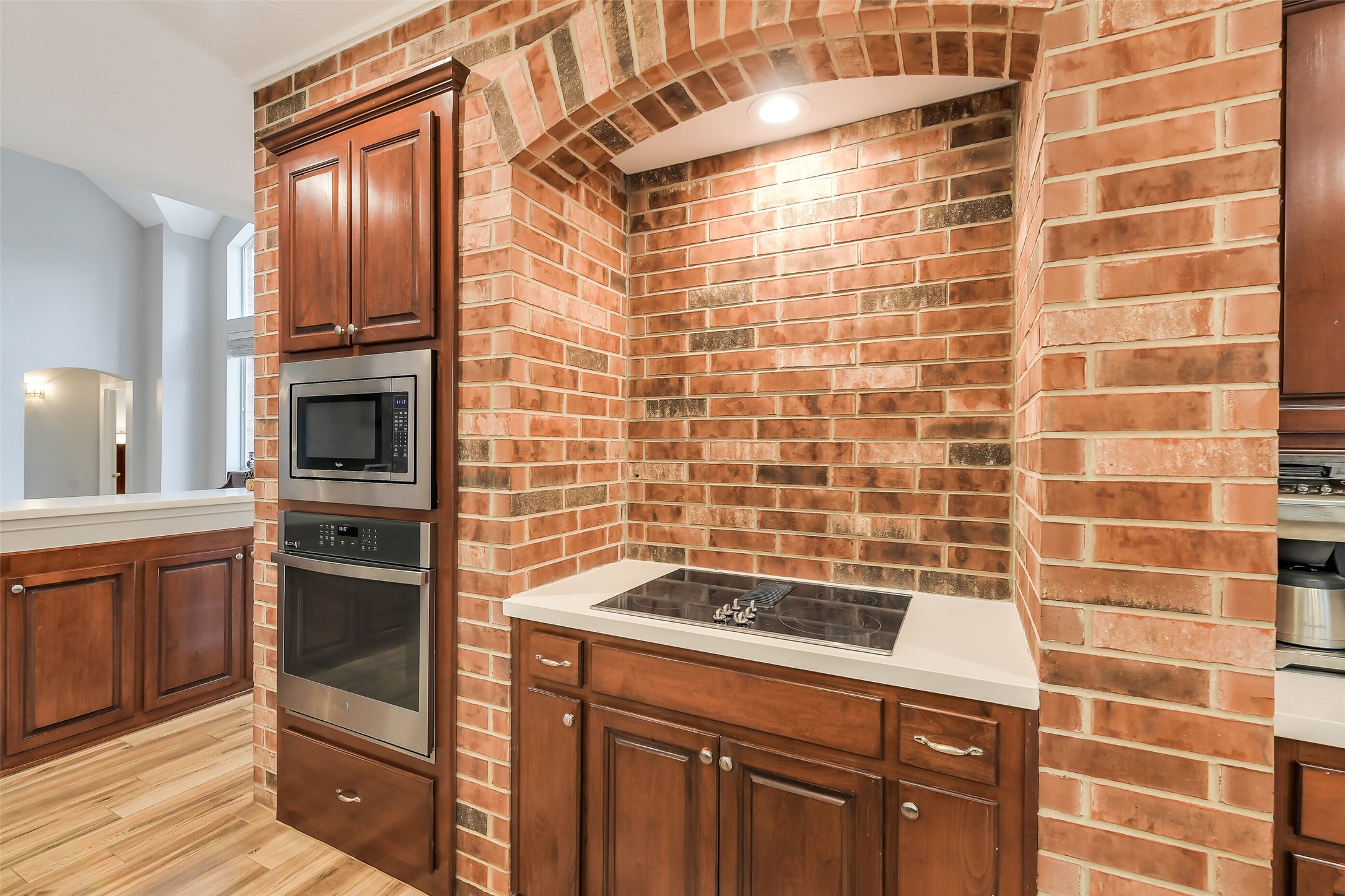 Elegant kitchen nook features a built-in cooktop set against a charming brick archway, complemented by rich wooden cabinetry and stainless steel appliances.