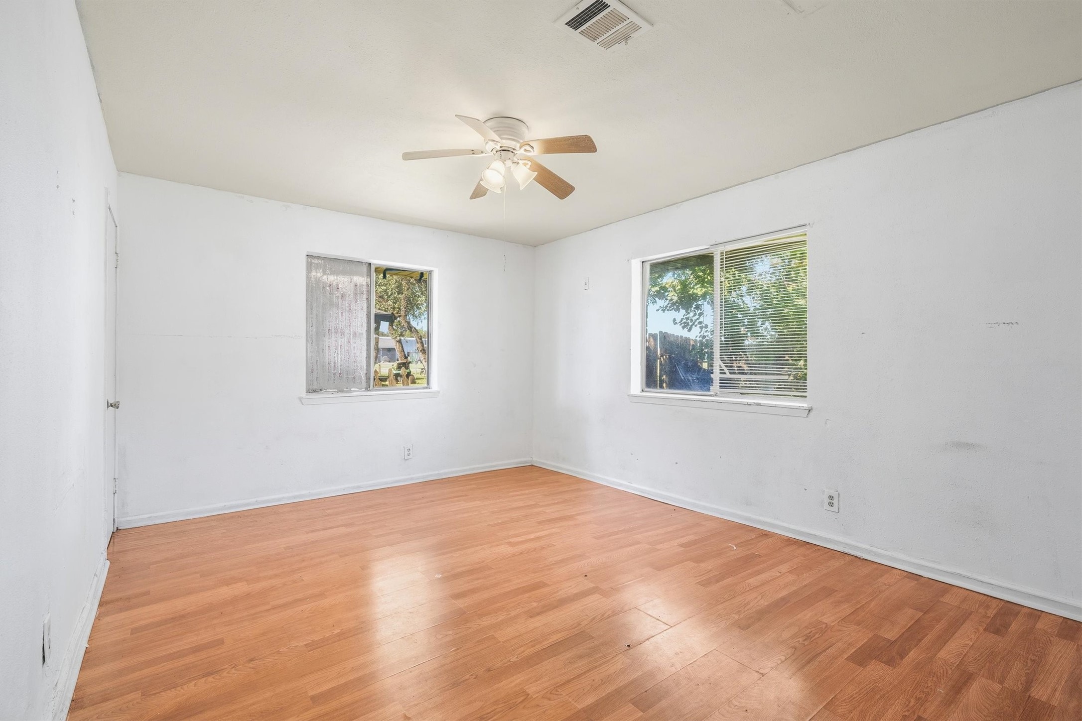 This spacious bedroom features wood flooring, a classic ceiling fan, and multiple windows, creating a comfortable and inviting retreat.