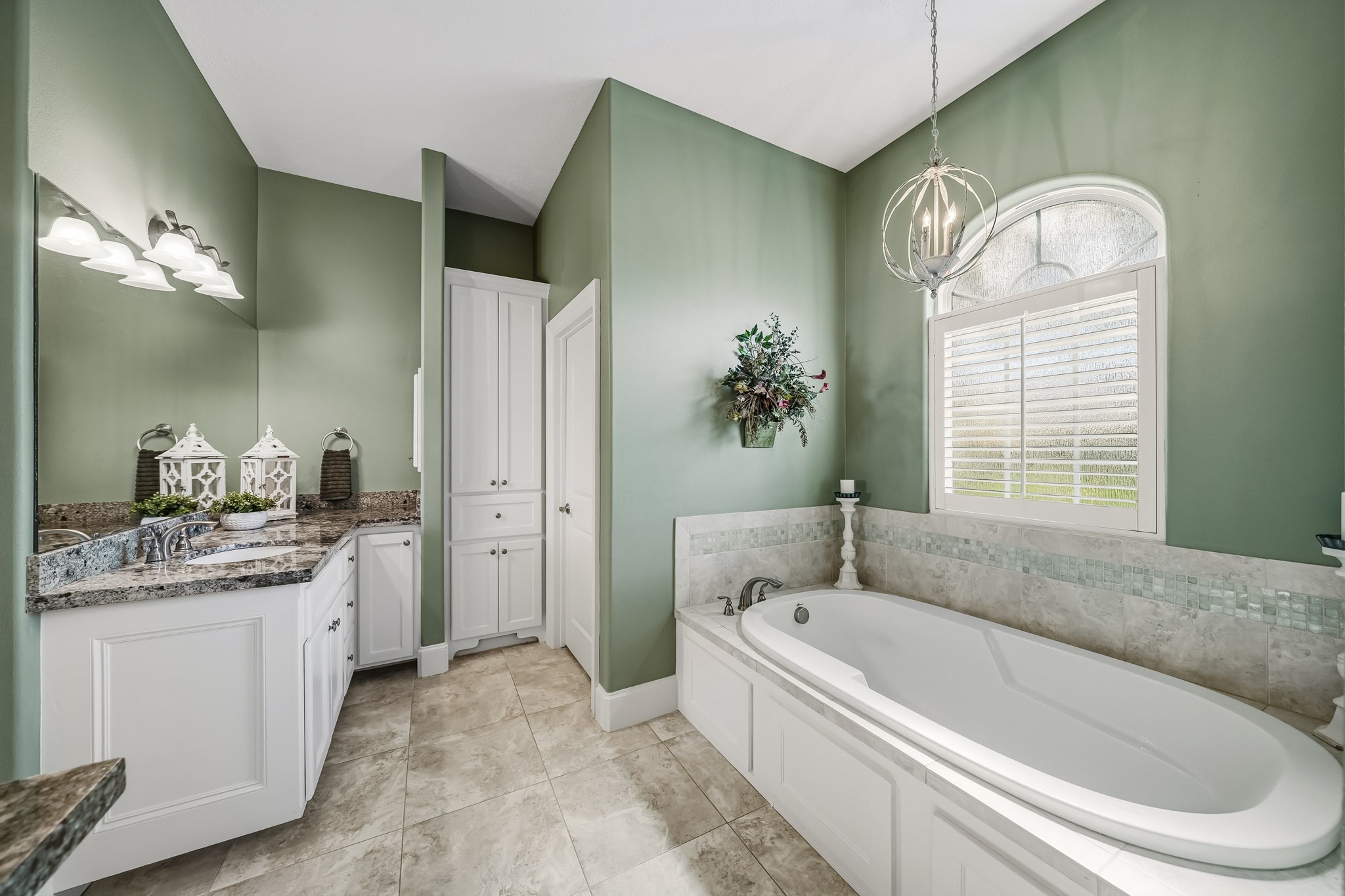 Indulge in a restorative escape within the oversized soaking tub, where soft mood lighting sets the stage for relaxation and rejuvenation. Overhead, an elegant arched transom crowns the window, adding architectural charm and inviting natural light into the space. Plantation shutters offer effortless privacy control, creating a serene sanctuary designed for quiet moments of luxury.