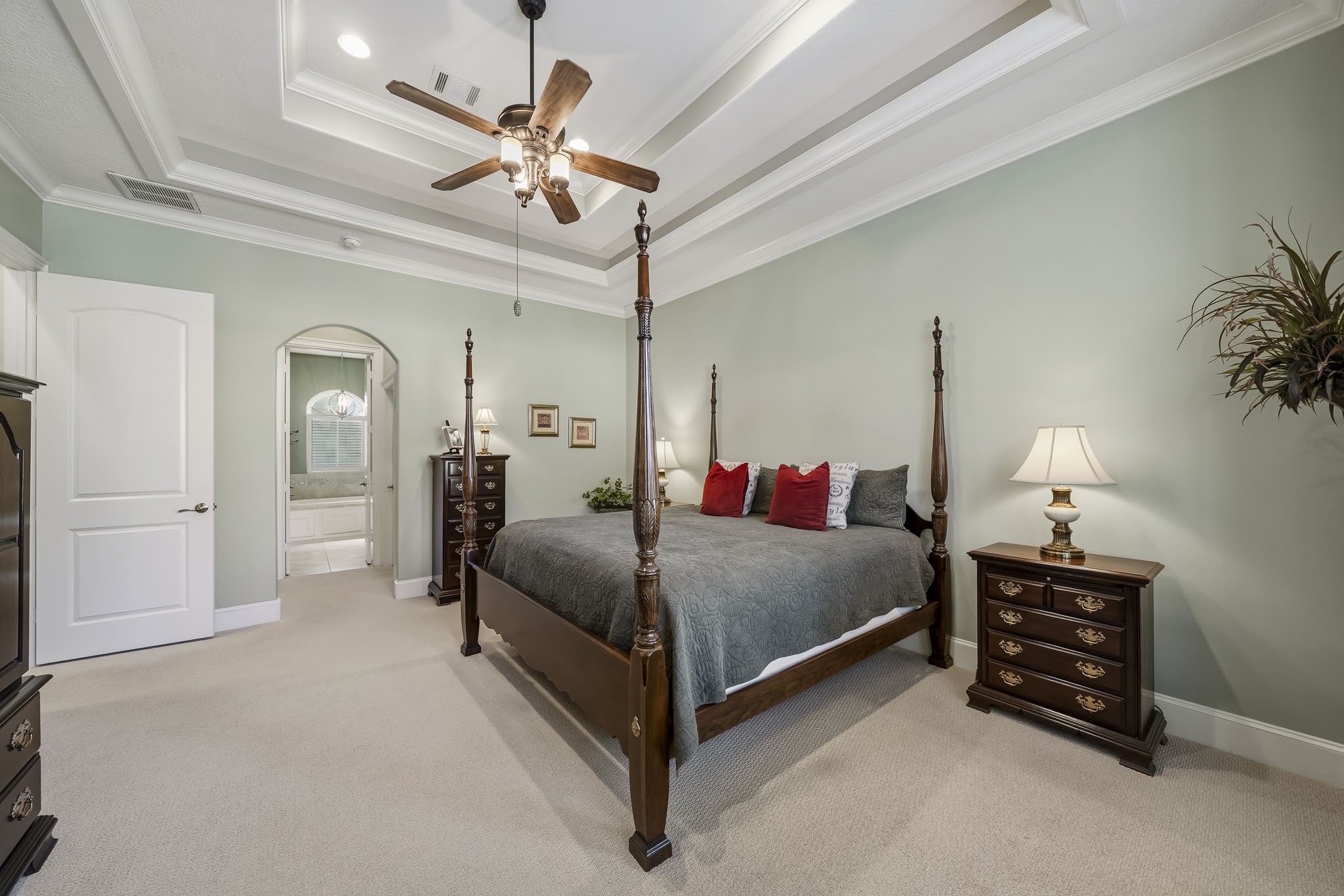 This spacious Primary Bedroom exudes comfort and sophistication, featuring plush carpeting underfoot, a soothing green palette, elegant crown molding, and a striking double tray ceiling that draws the eye upward and enhances the room's sense of scale.