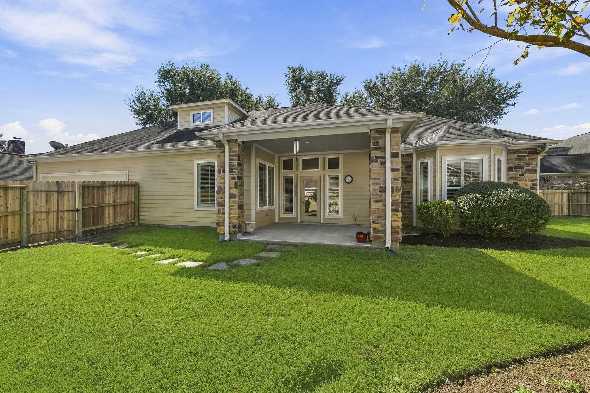 The Back Patio is easily accessed from the Family Room through the glass-paneled door shown here, creating a seamless connection between indoor and outdoor living. With ample space for an outdoor dining table or a cozy conversational seating arrangement, this inviting retreat is perfectly suited for al fresco meals, morning coffee, or evening relaxation. A charming stone pathway leads through the gate and onward to the home's 2-car Garage, adding both beauty and convenience to the outdoor space.