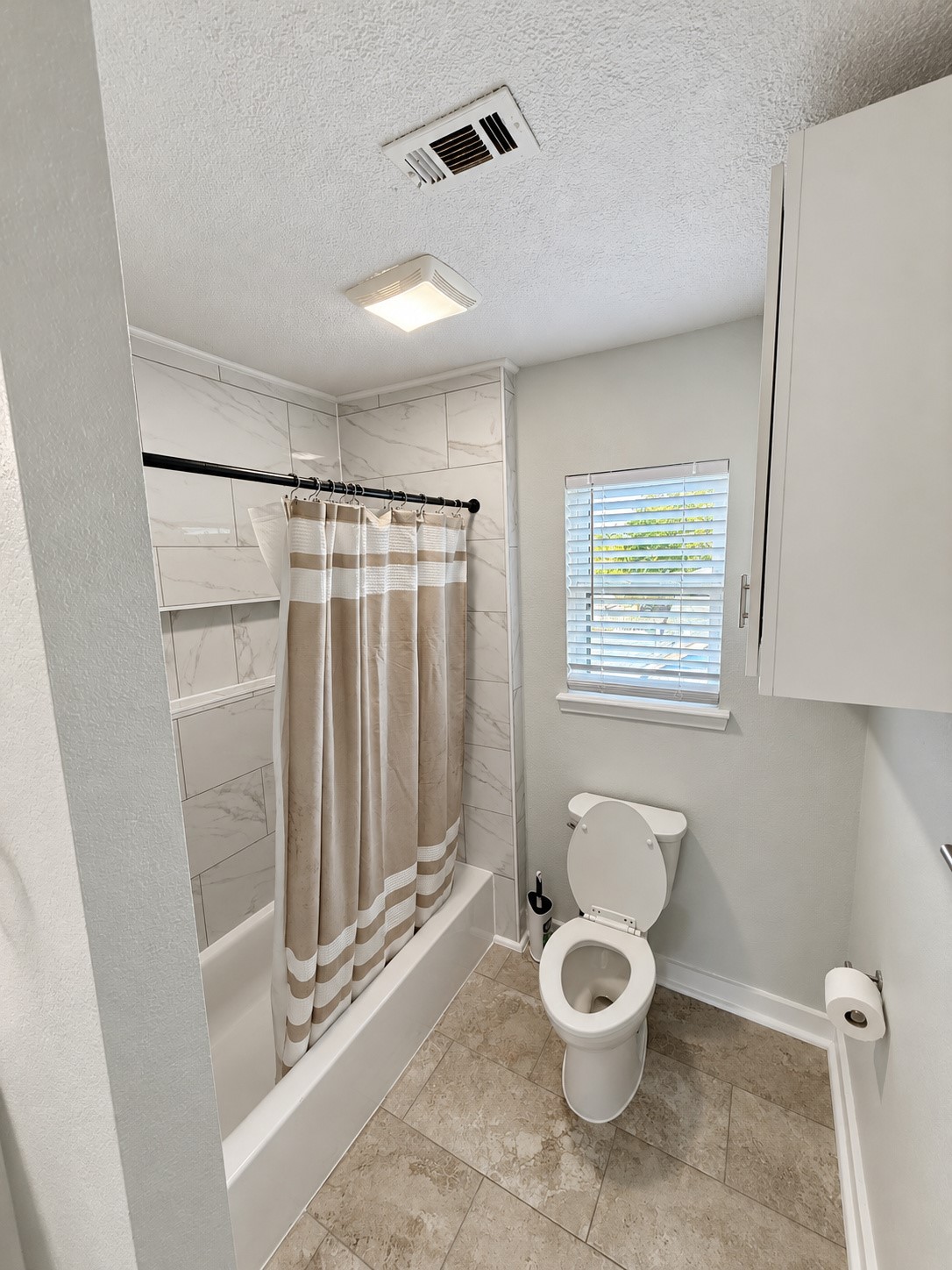 Bathroom with natural light, overhead storage, and a tiled tub/shower surround.