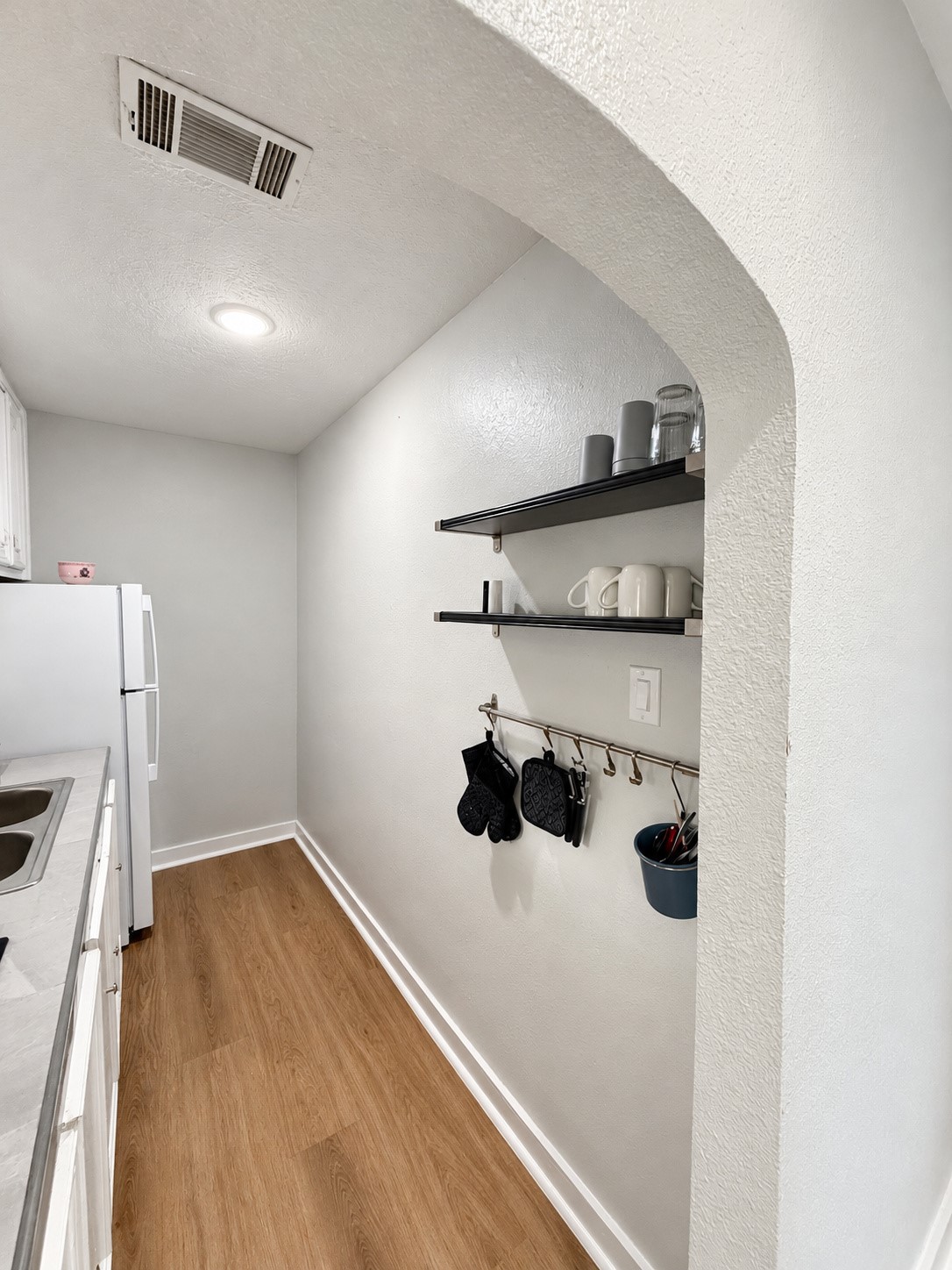 Galley kitchen with white cabinetry, open shelving, and wood-look flooring.