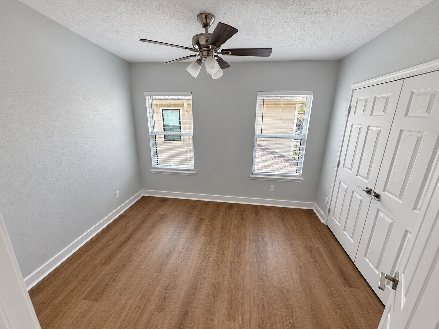 Bedroom with two windows, wood-look flooring, a ceiling fan, and a double-door closet.