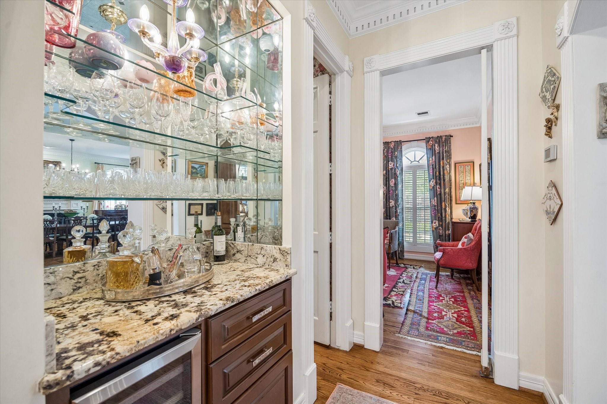The dry bar is conveniently situated between the formal living room and the kitchen. Glass shelves, a mirror backing, and granite countertop complement the space. The bar also features a wine refrigerator and storage.