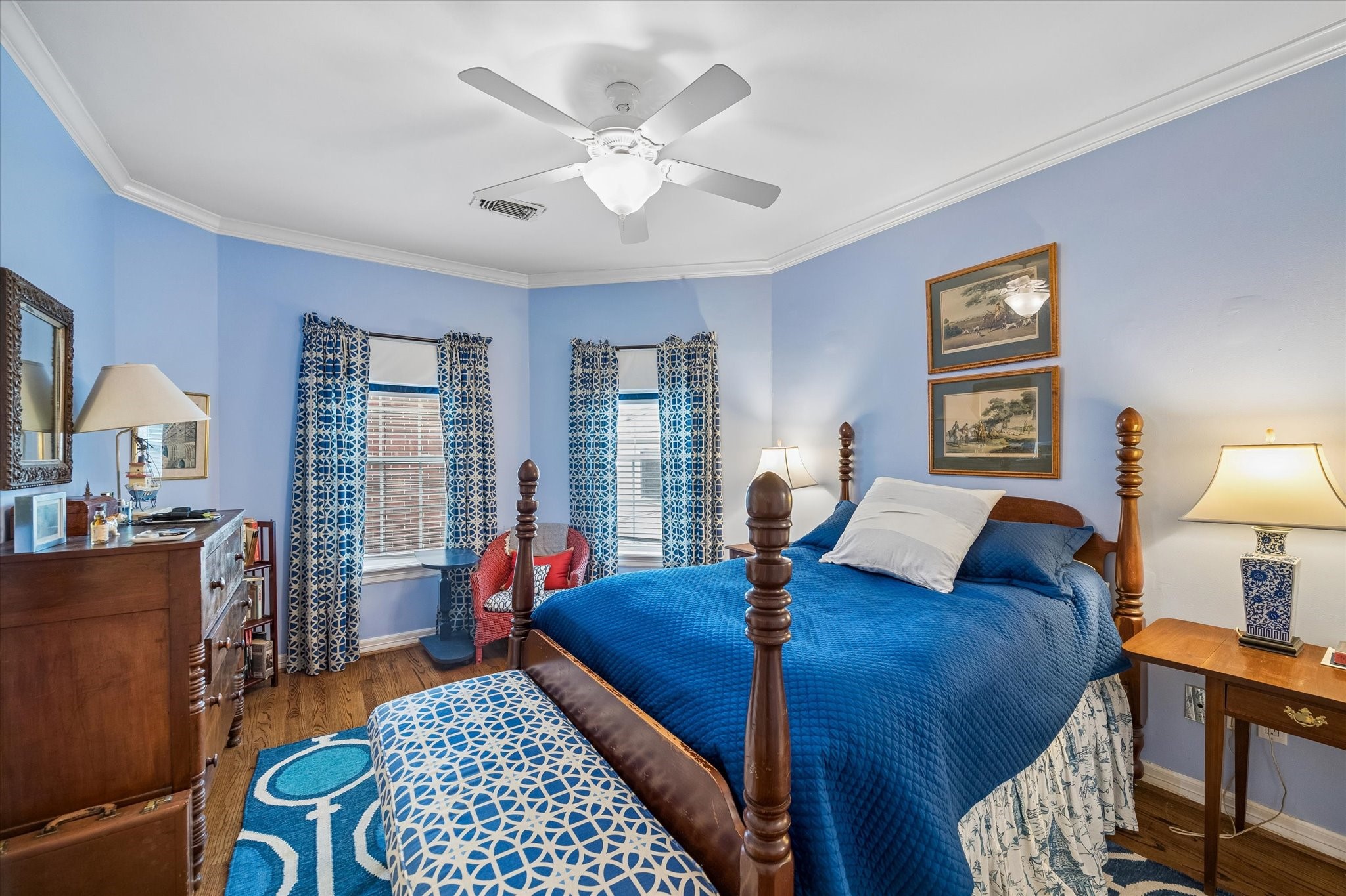 This secondary bedroom features an airy light blue walls, large closet, an en-suite bathroom, hardwood floors, and crown molding.