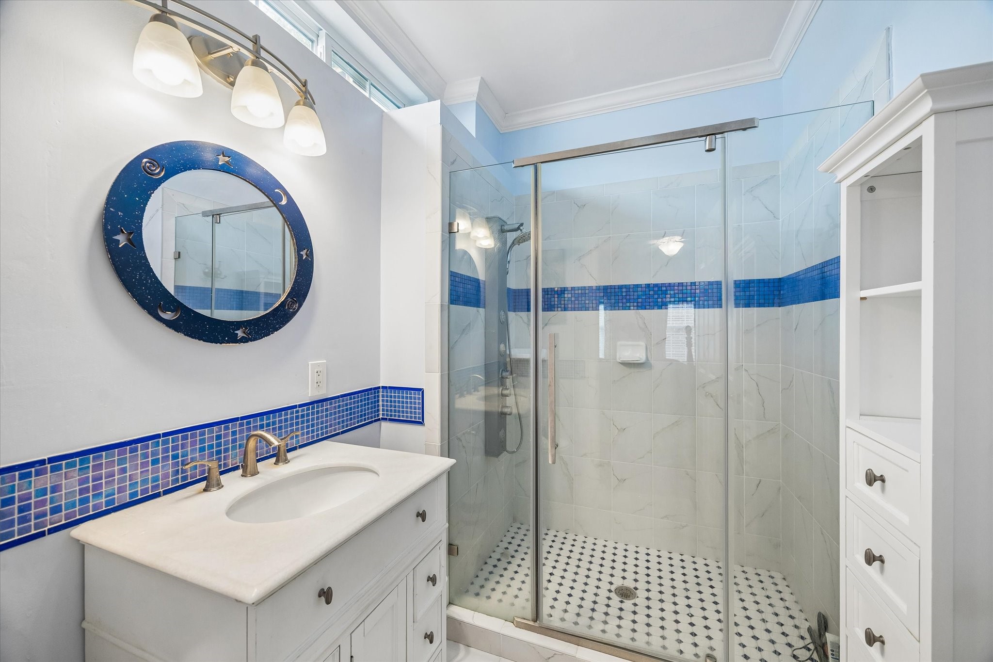 Gorgeous en-suite! Features a large standing shower, blue tile accents, and windows just below the ceiling to bring in natural light without sacrificing privacy.