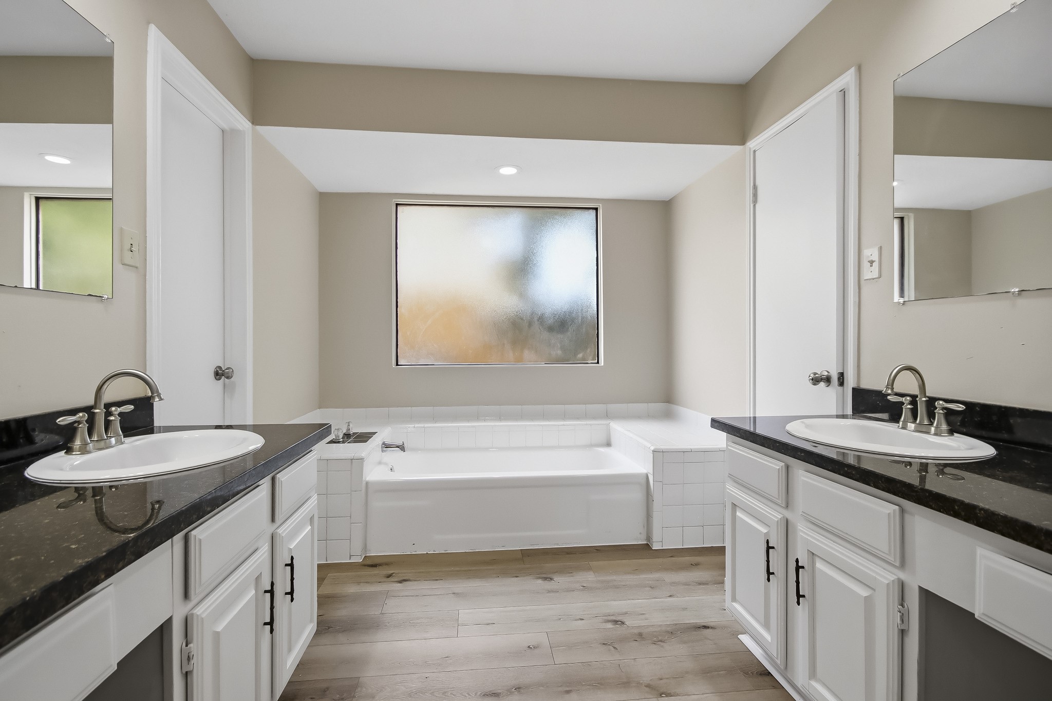 Primary ensuite bathroom featuring dual vanities, dark countertops, and a soaking tub.