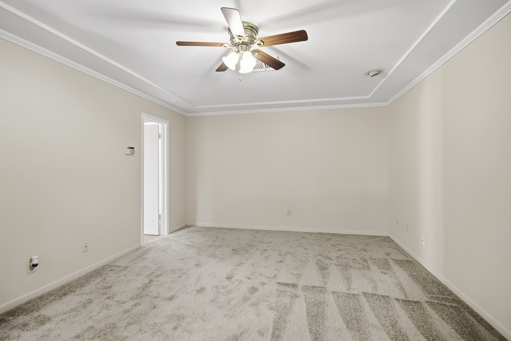 Spacious primary bedroom featuring a tray ceiling, crown molding, and ceiling fan. Brand new carpet!