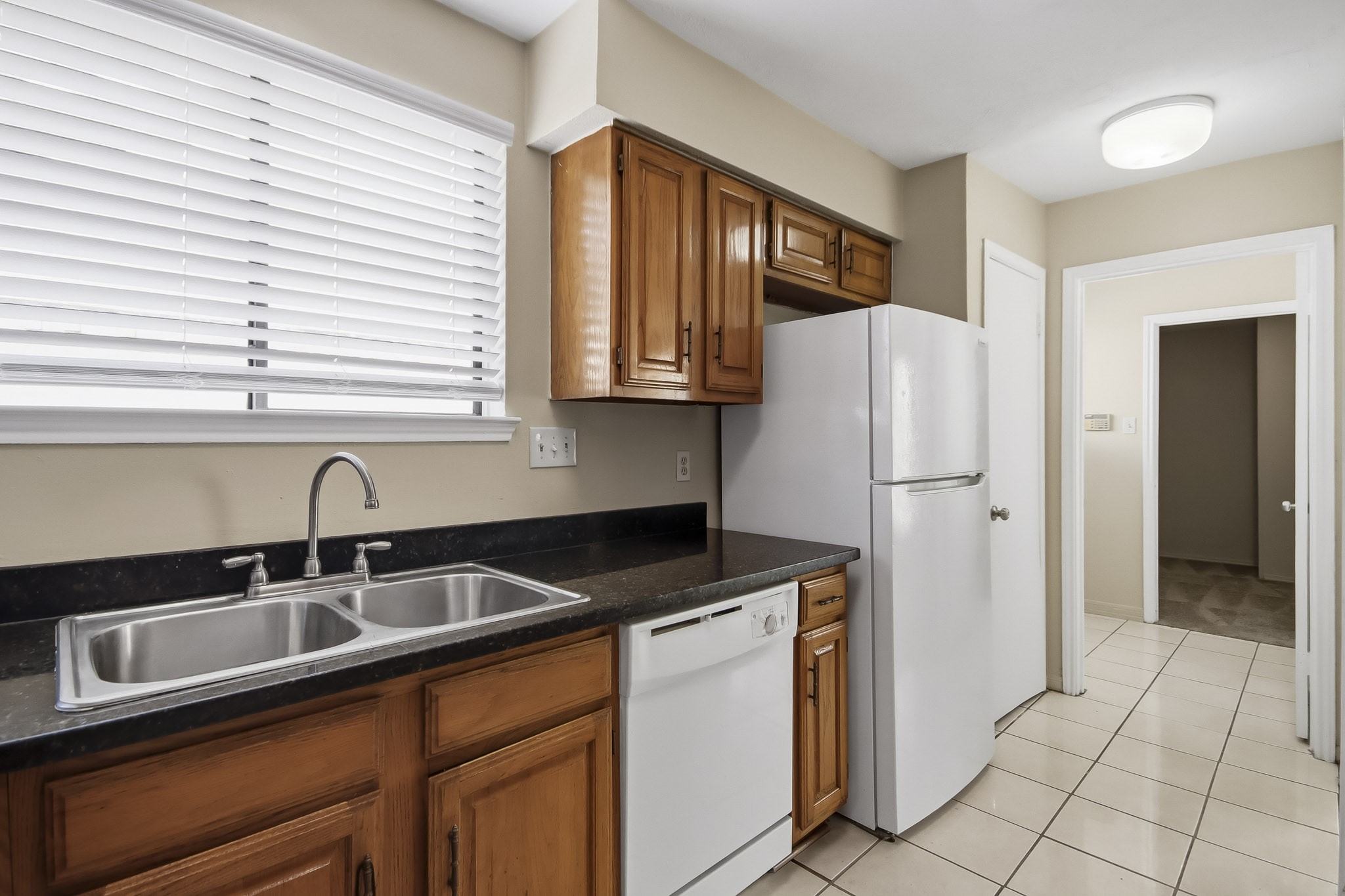 Kitchen featuring wood cabinetry, dark countertops, a double sink, and tile flooring.
