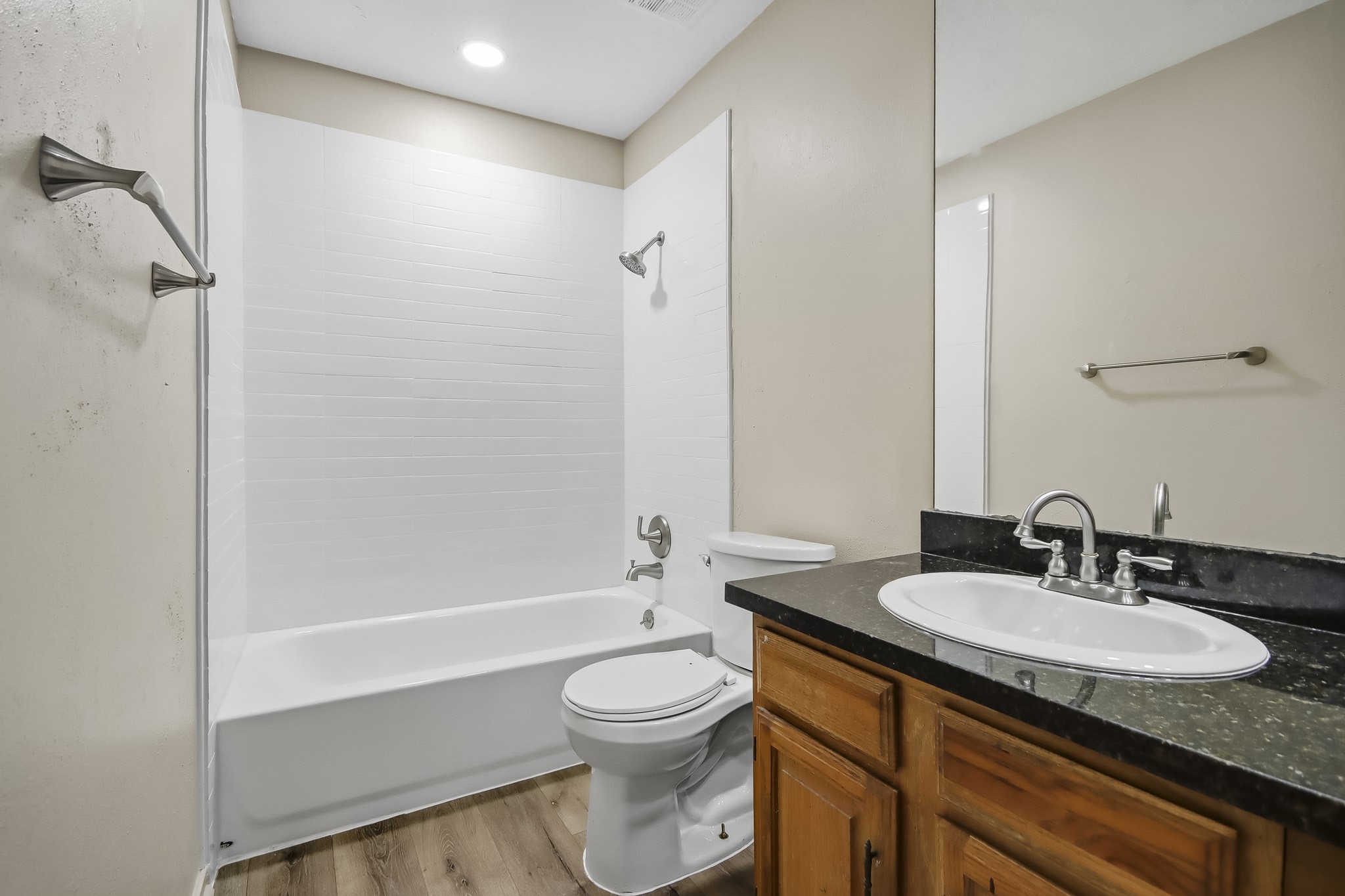 Shared bathroom featuring a tub and shower combination, single vanity, and wood-look flooring.