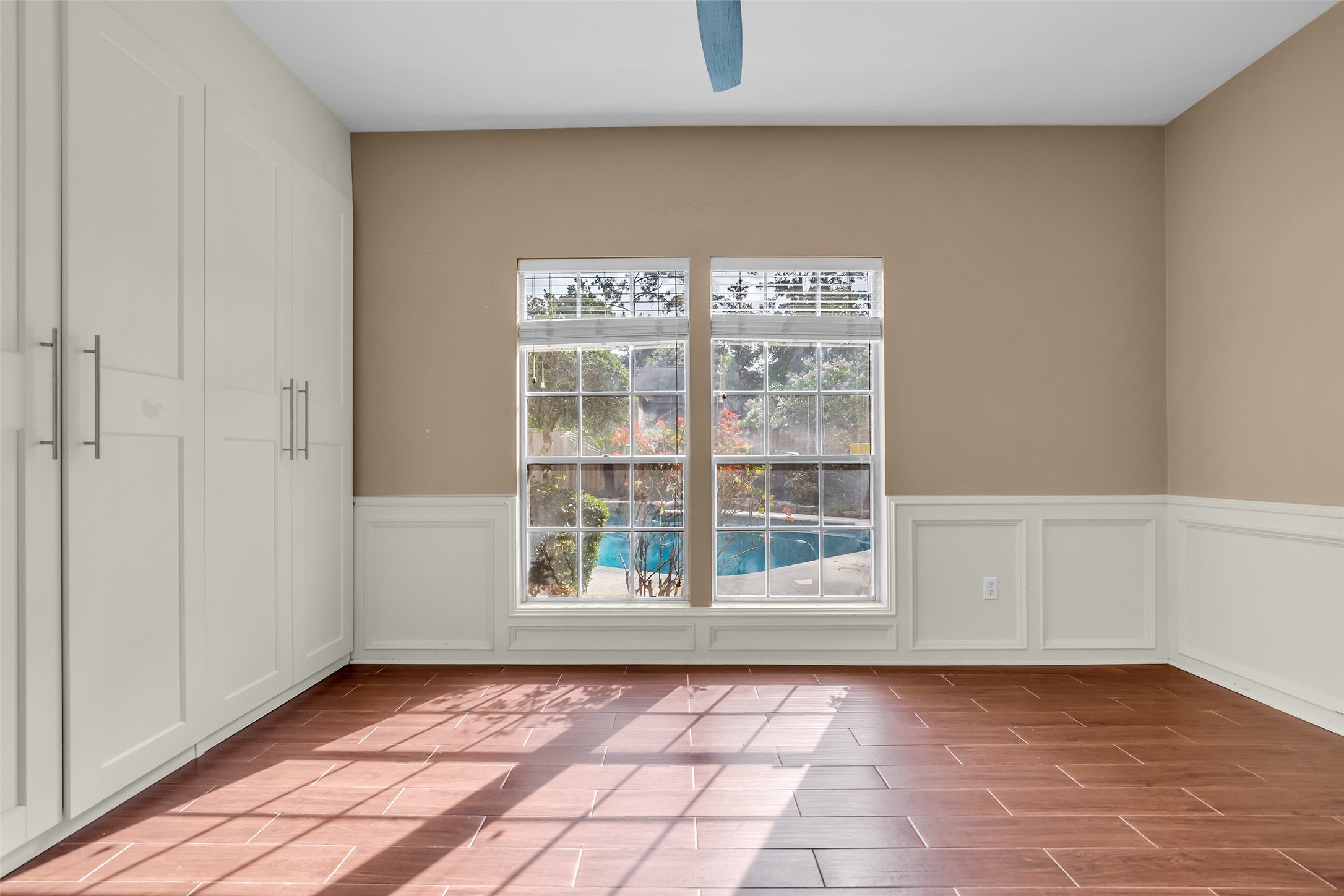 Secondary bedroom on the first floor featuring large windows with views of the backyard pool, allowing ample natural light to fill the space throughout the day.