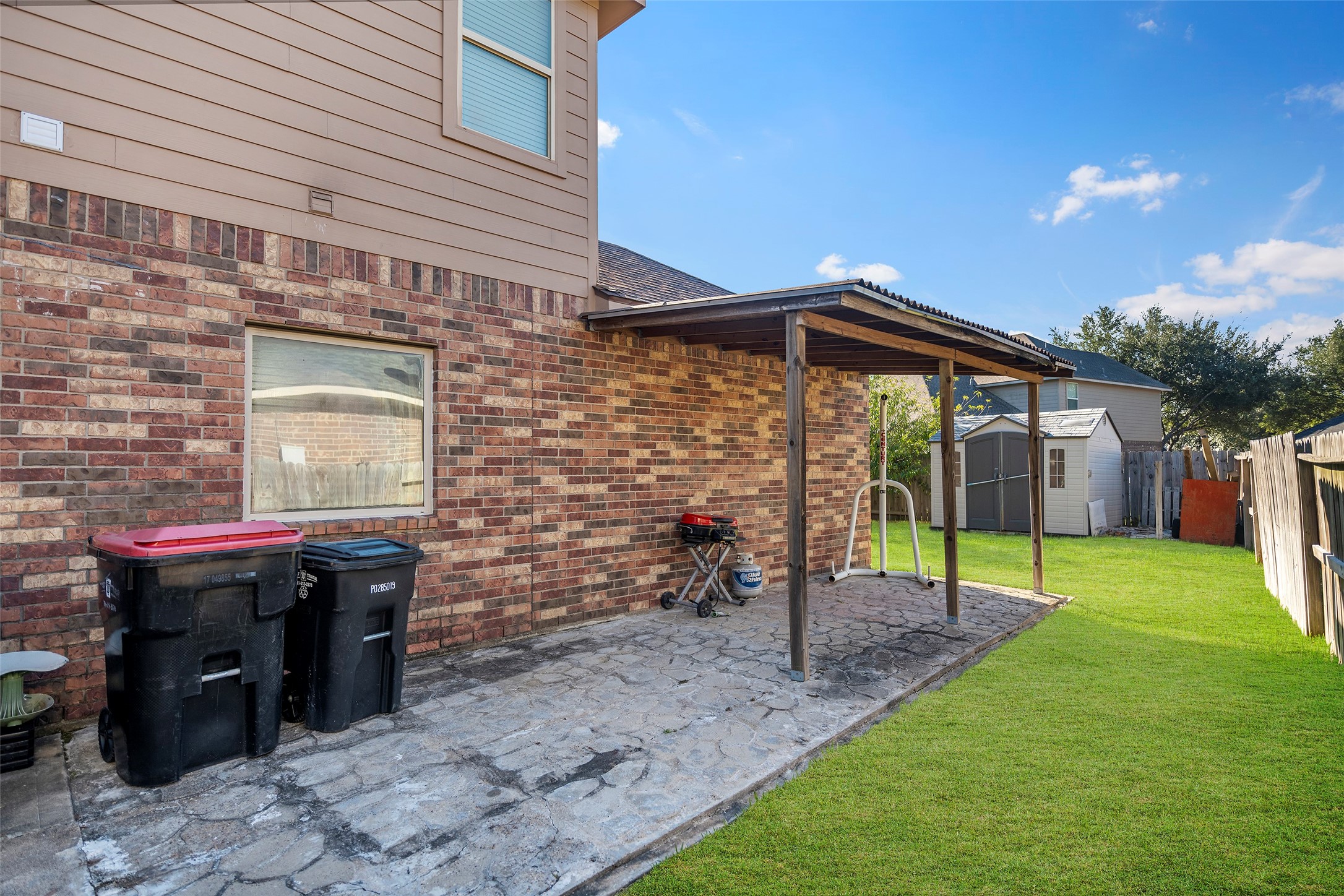 Side patio and additional storage shed included with the property. Note: The grass in this photo has been virtually enhanced to demonstrate the property's full potential.