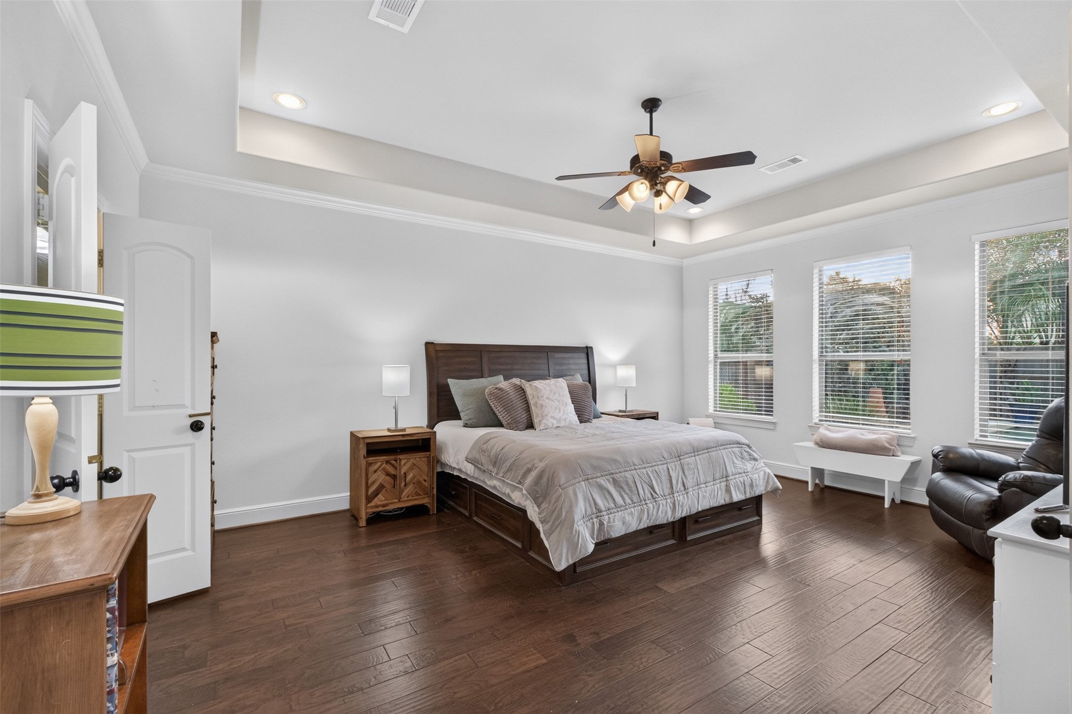 Primary bedroom featuring hardwood floors, tray ceiling, crown molding and a fabulous backyard view
