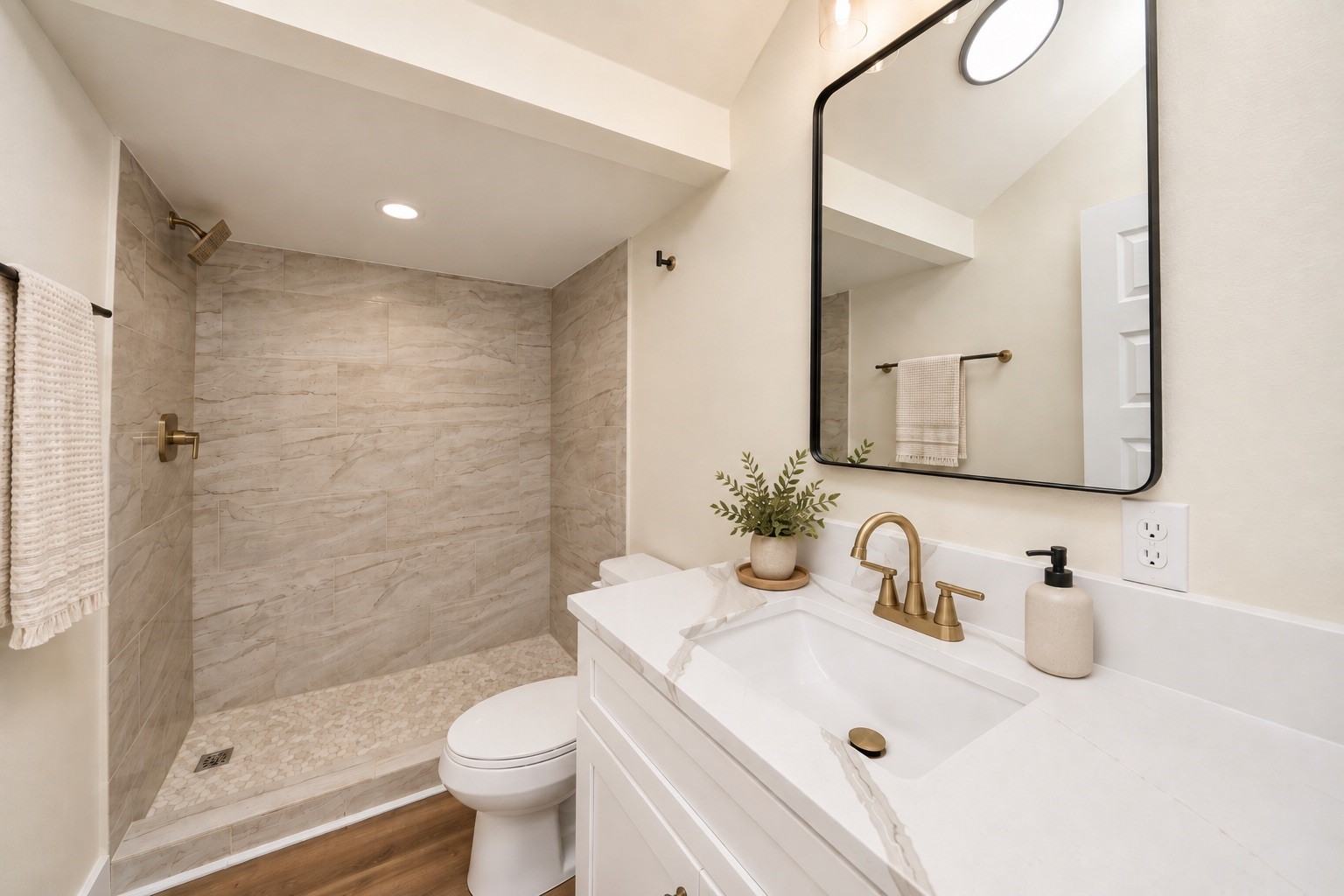 Convenient first-floor full bathroom featuring a spacious walk-in shower with decorative tile surround, quartz vanity countertop, framed mirror & modern fixtures.
