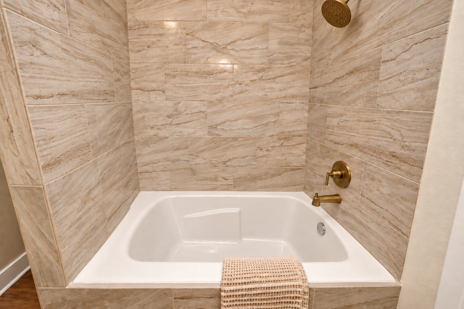 Close-up of the primary bathroom's soaking tub and shower combination, featuring beautiful floor-to-ceiling tile, elegant gold-tone fixtures & a spacious bathing area.