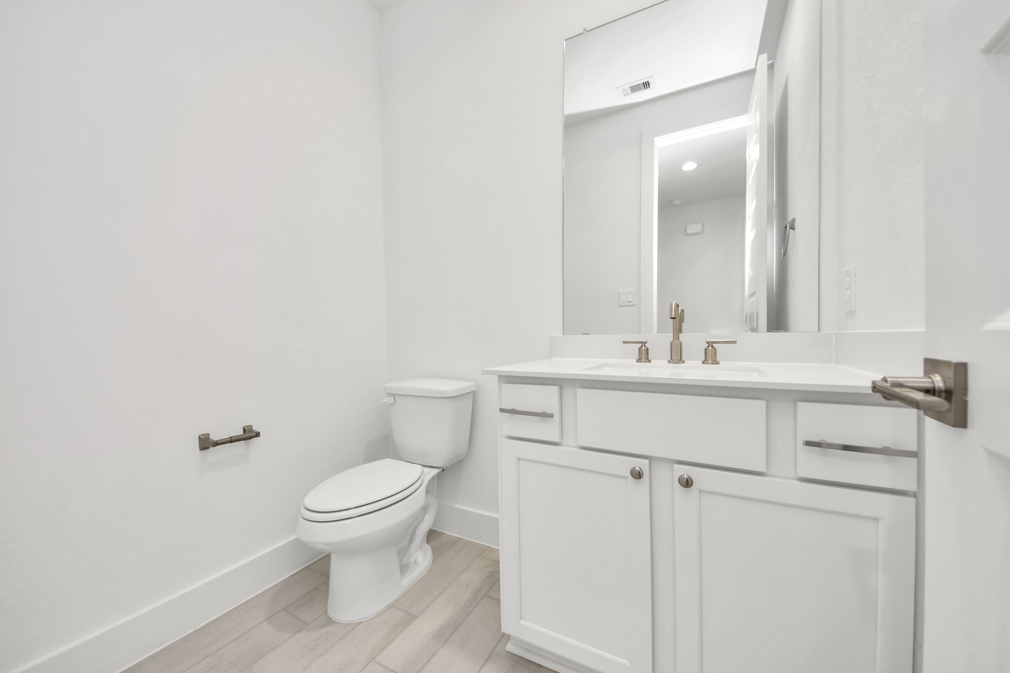 Sophisticated half bathroom adorned with contemporary finishes. The elegant 5-panel door welcomes you to a space where style meets functionality. Notice the sleek hardware accents that add a touch of modern charm. The vanity boasts light-colored countertops, beautifully complemented by a tasteful vanity light, creating a well-lit and inviting atmosphere. Sample photo of completed home with similar floor plan. Actual colors and selections may vary.