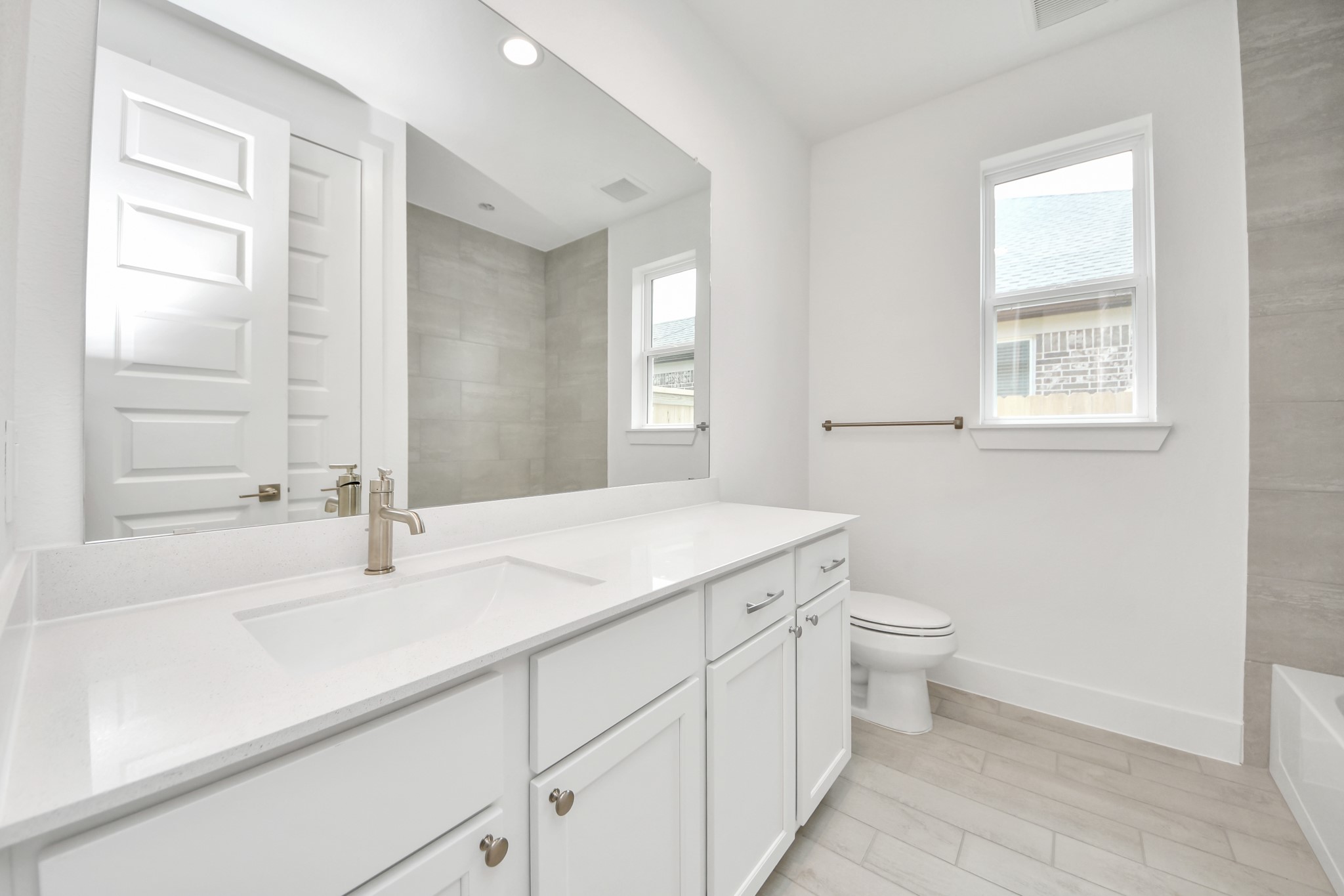 Secondary bath features tile flooring, walk-in shower with tile surround, light stained wood cabinets, beautiful light countertop. Sample photo of completed home with similar floor plan. Actual colors and selections may vary.