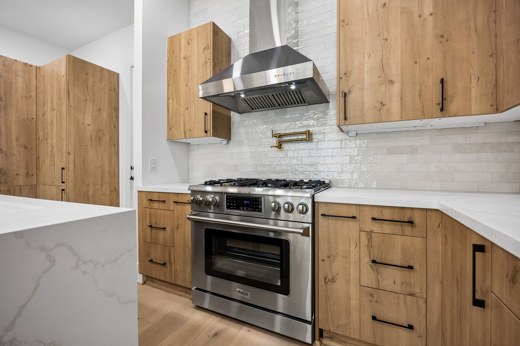 Kitchen  offers a stainless steel gas range, chimney-style vent hood, pot filler and full-height tile backsplash.