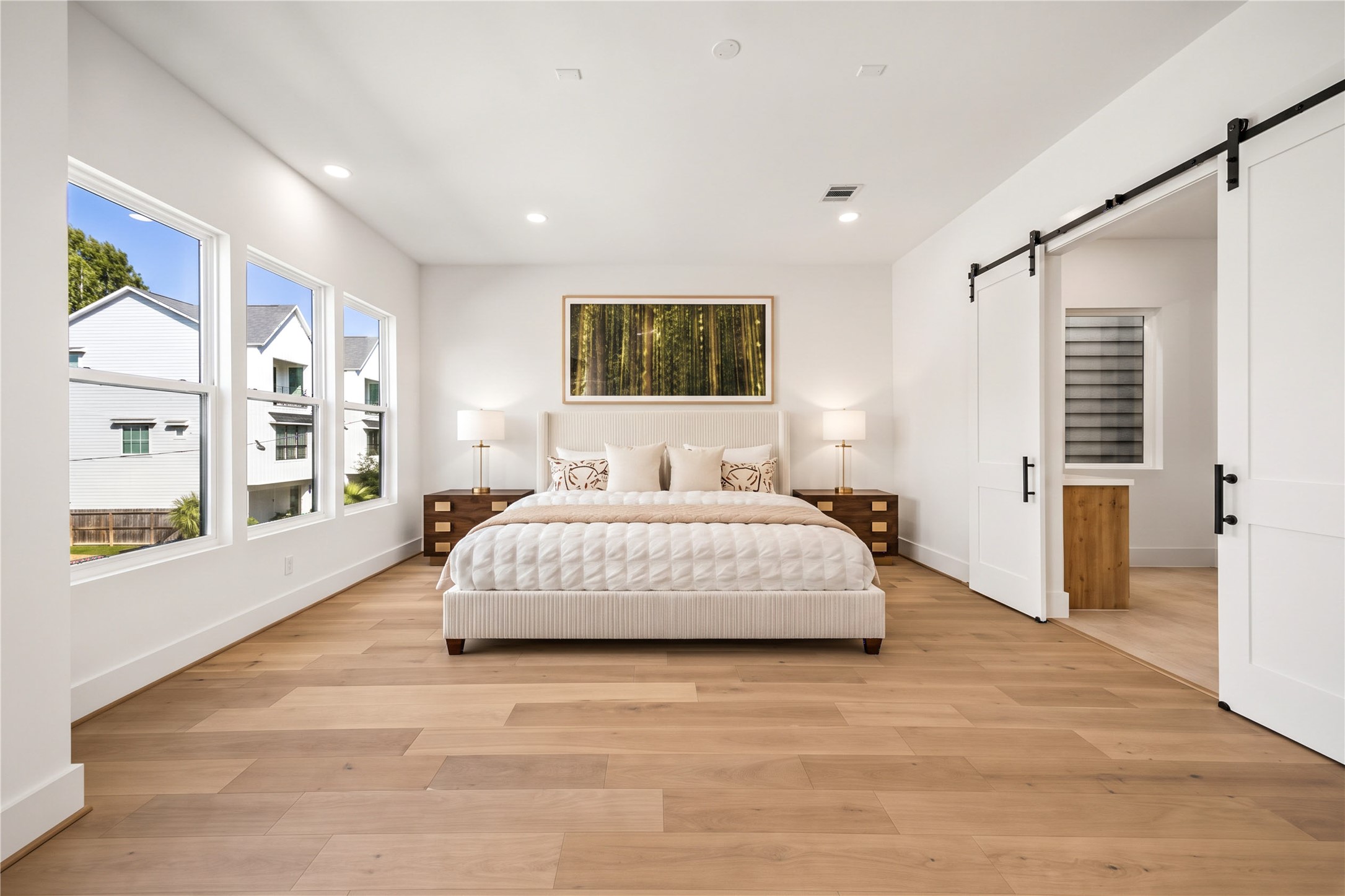 Primary suite  spacious retreat featuring wood flooring, recessed lighting and a sliding barn door. (virtual staging)