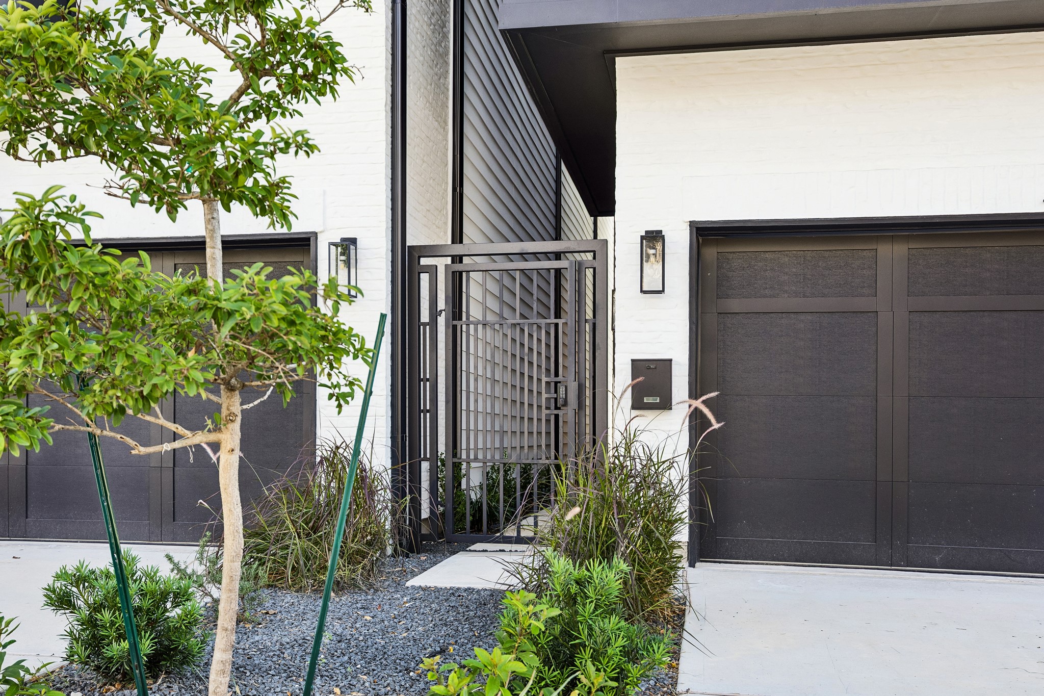Gated front entry  features lush landscaping, modern lantern lighting and a sleek garage door.