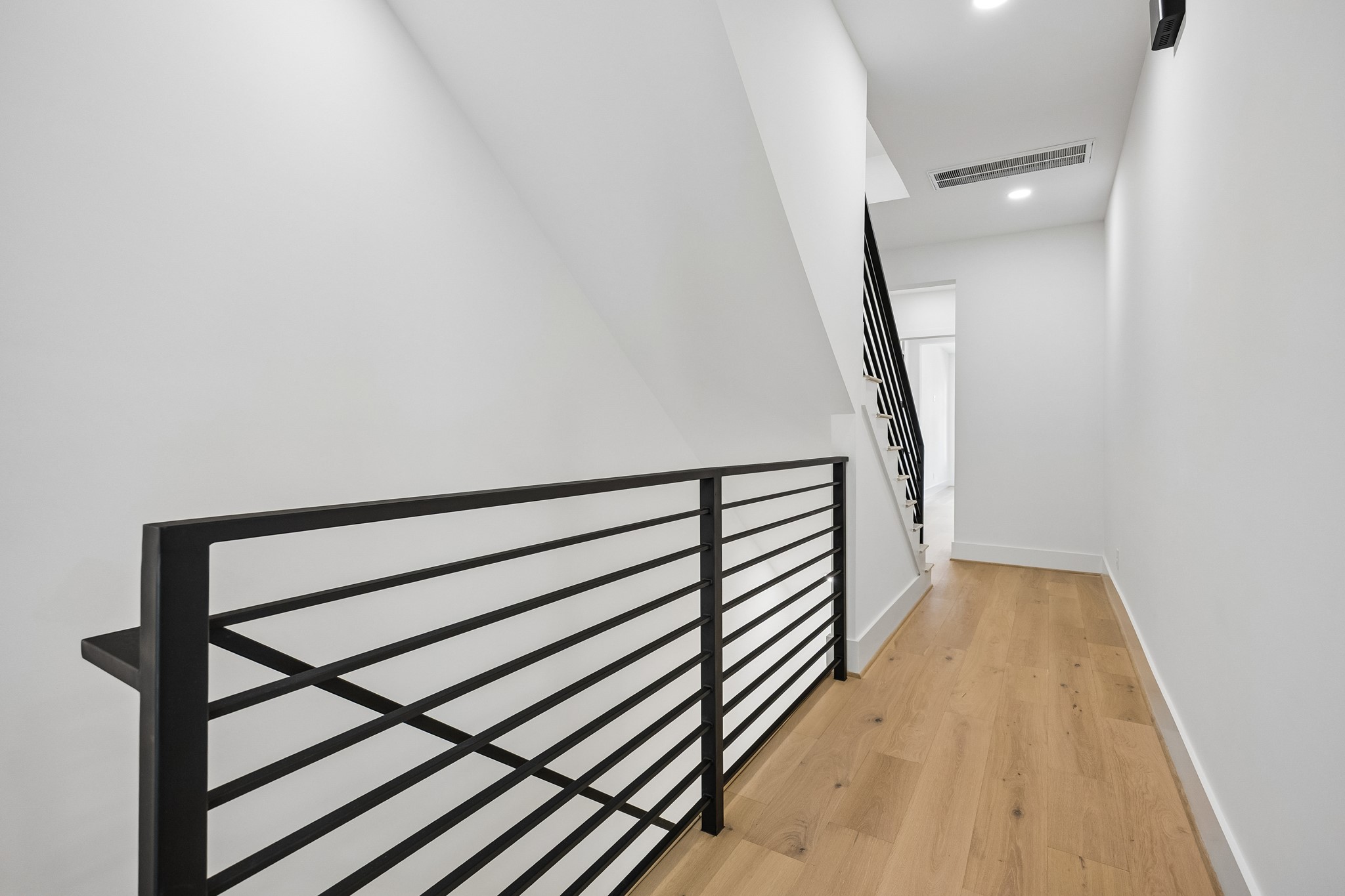 Second-floor landing  features modern black metal railings and wood flooring.