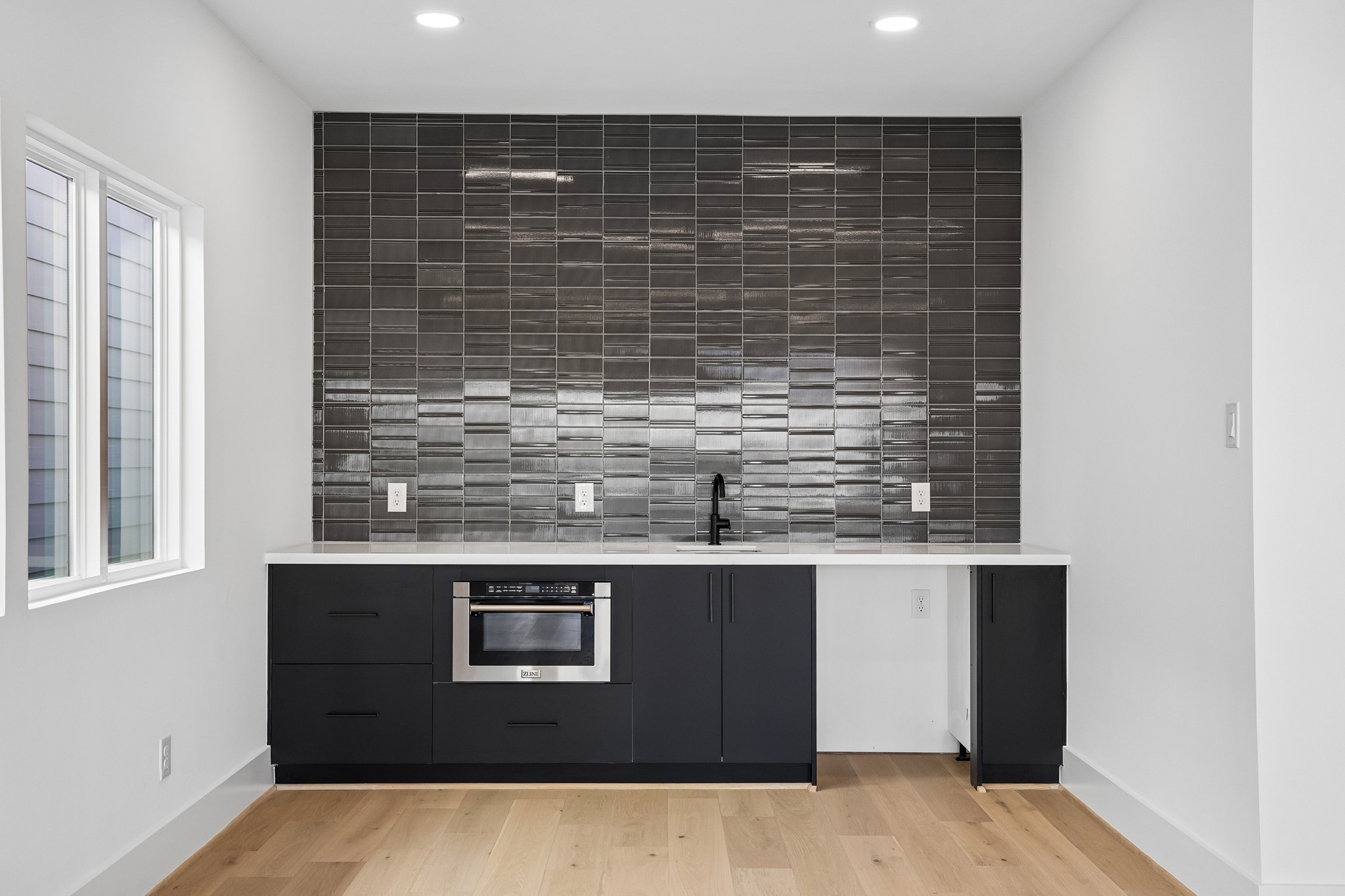 Entertainment bar  features custom cabinetry, an undermount sink, built-in microwave and dramatic tile backsplash.