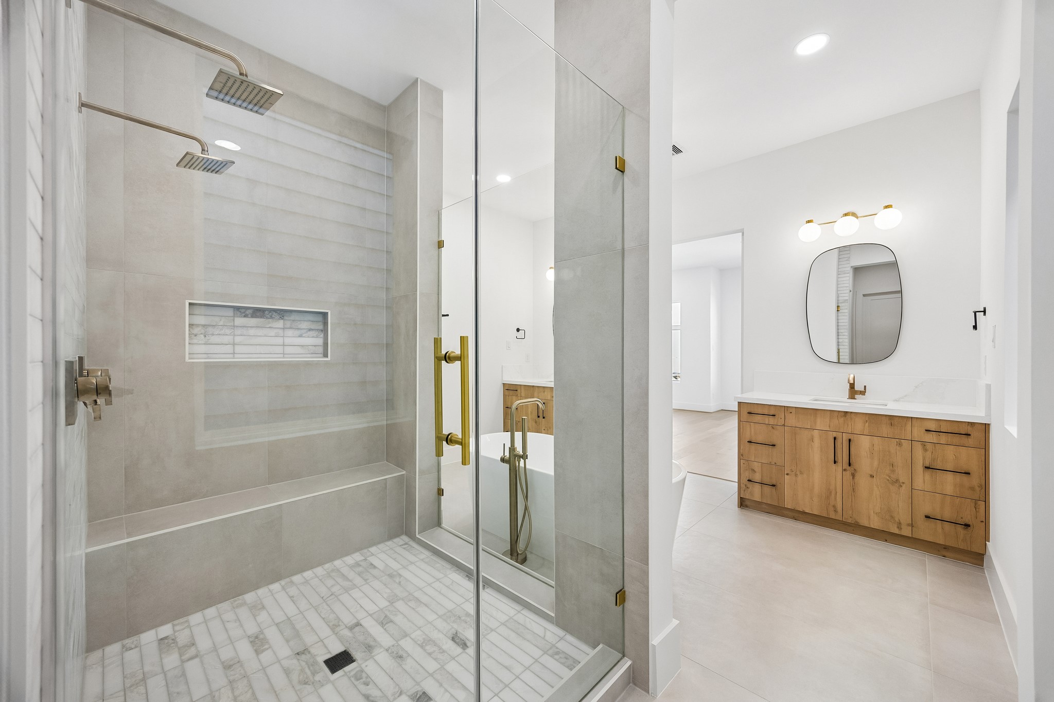 Primary shower  features a frameless glass enclosure, rain showerhead, built-in bench, and tiled niche.