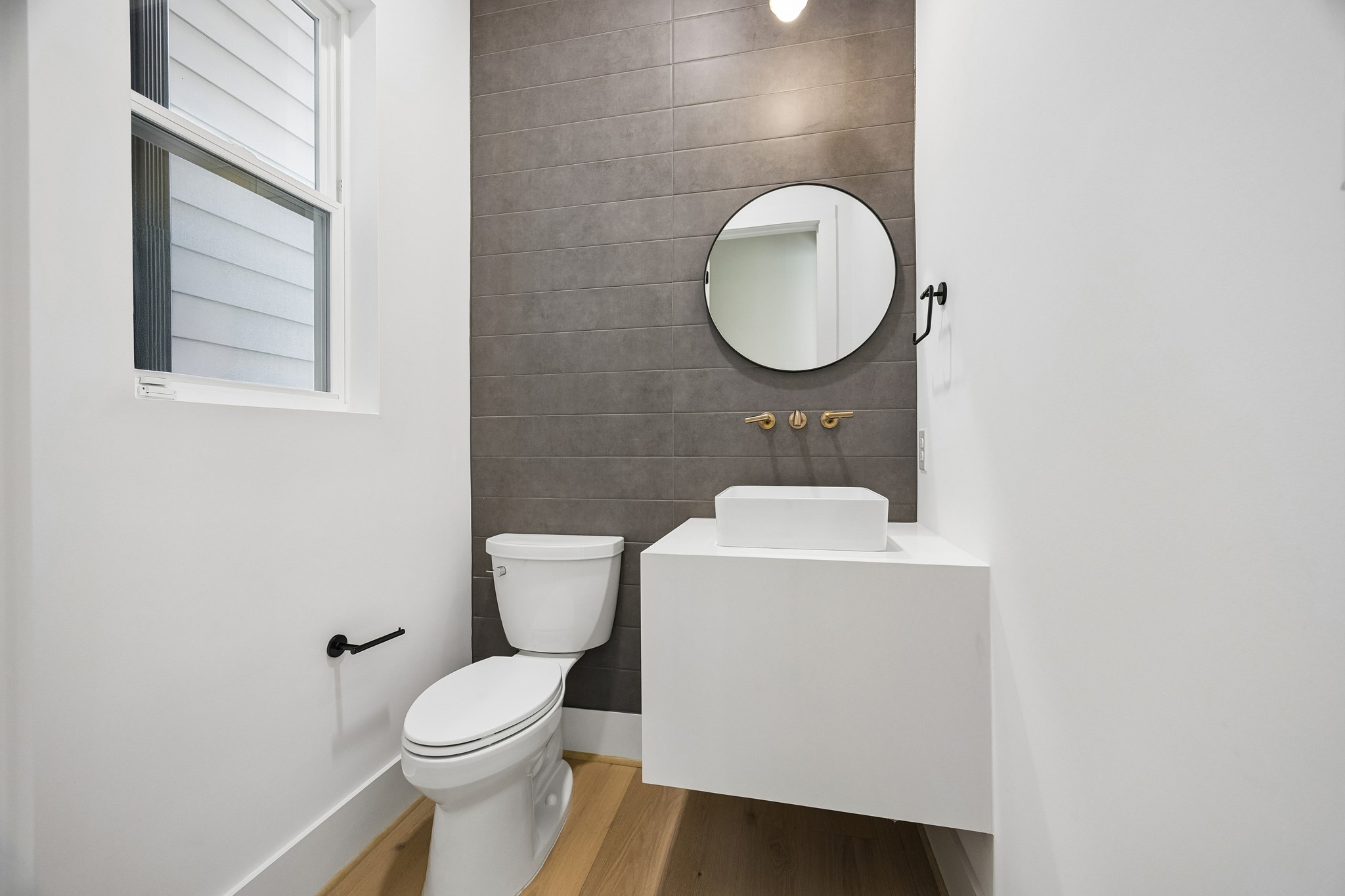 Powder room  features a floating vanity, round mirror, and tile accent wall.