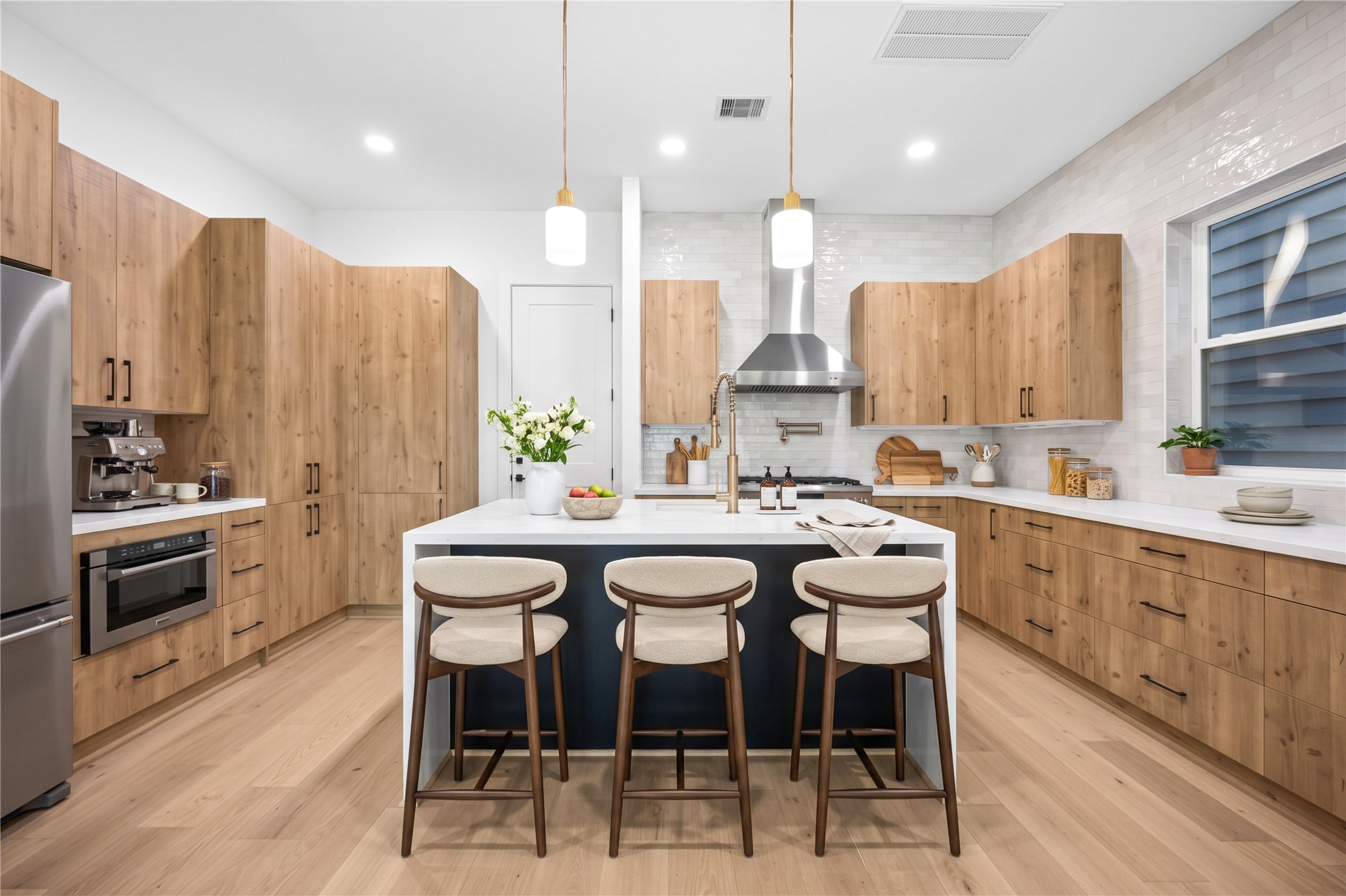 Kitchen  features a double edge waterfall island, custom wood-tone cabinetry, designer pendant lighting and quartz counters. (virtual staging)