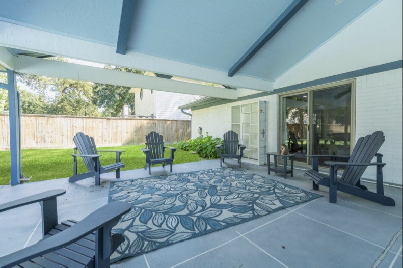 Covered outdoor seating area with a vaulted ceiling, exposed beams, and backyard views.