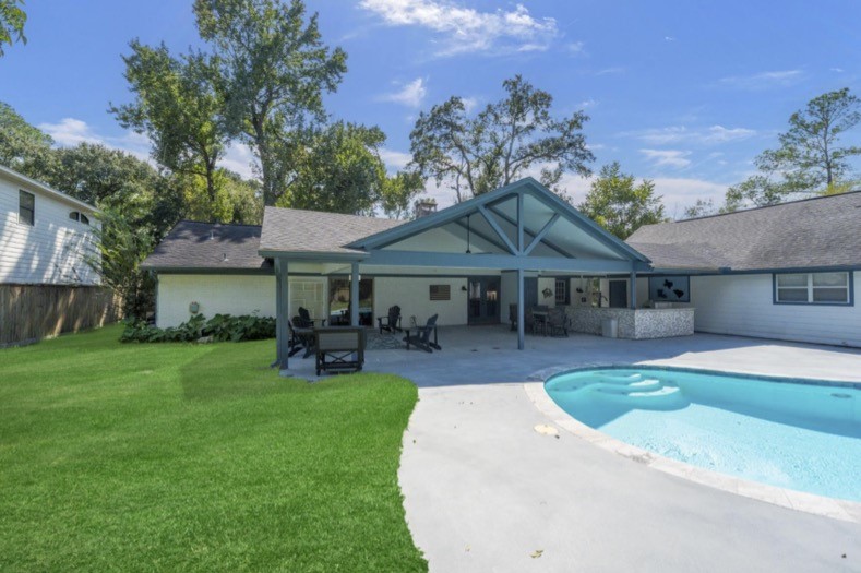 Rear view of the home showcasing the covered patio, outdoor kitchen, and pool.