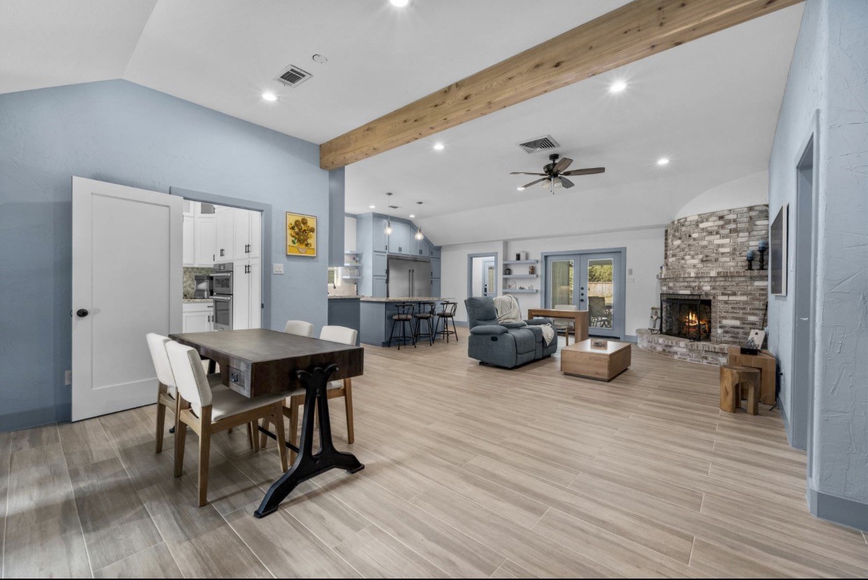 Open living and dining spaces feature a vaulted ceiling, exposed beam, and views toward the fireplace and kitchen.