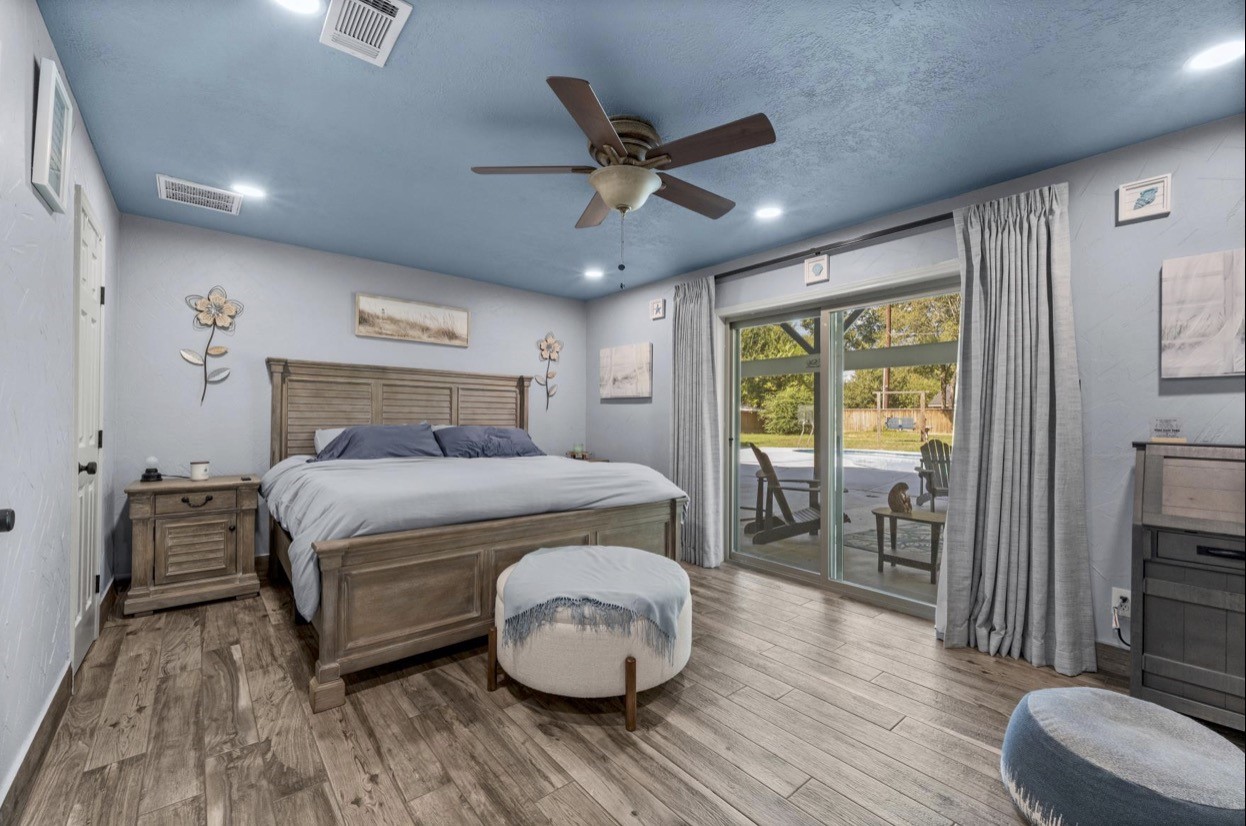 Primary bedroom with a blue accent ceiling, ceiling fan, and glass doors opening toward the patio.
