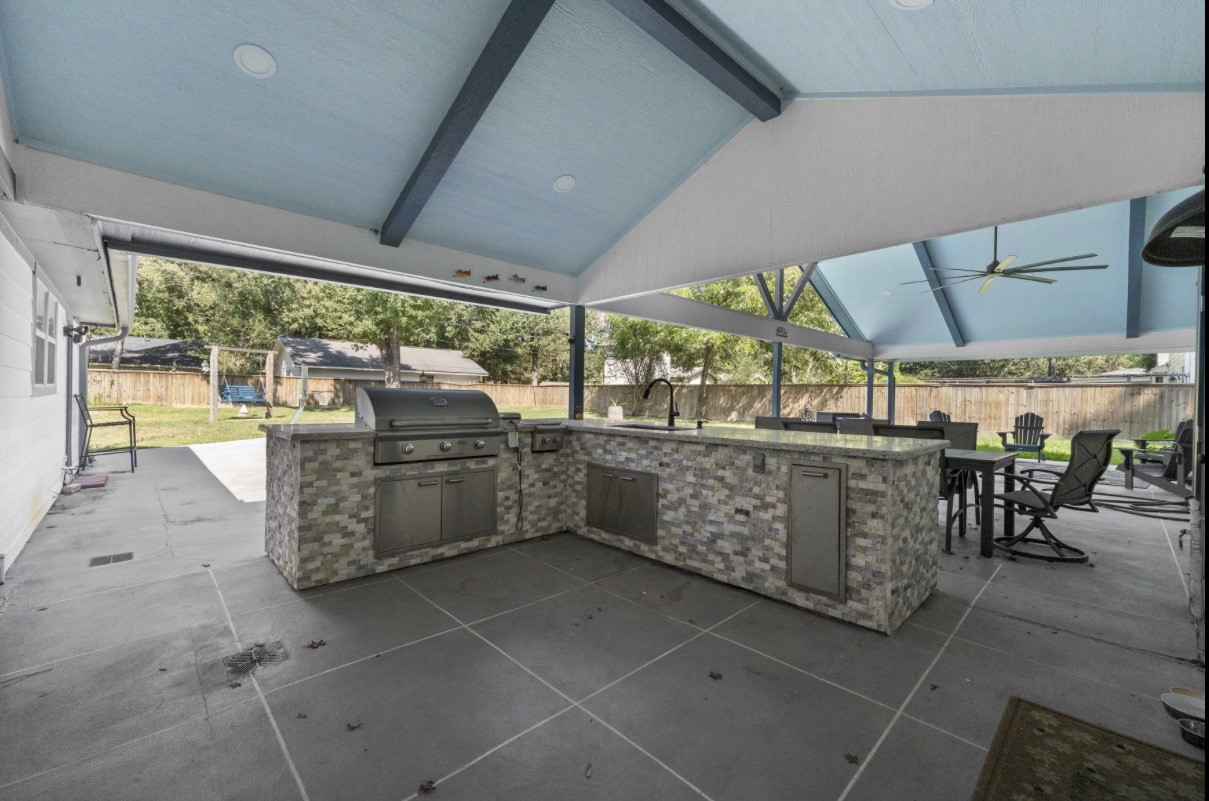 Covered outdoor kitchen with a built-in grill and space for dining and gathering.