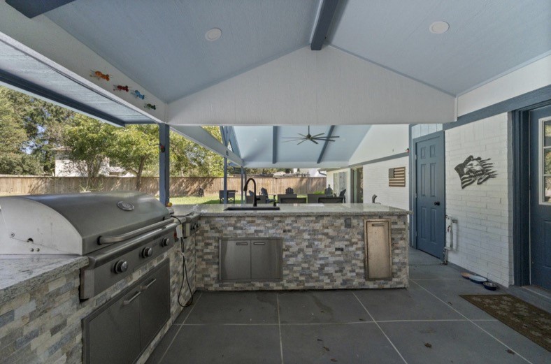 Outdoor kitchen with a built-in grill, sink, counter space, and storage.