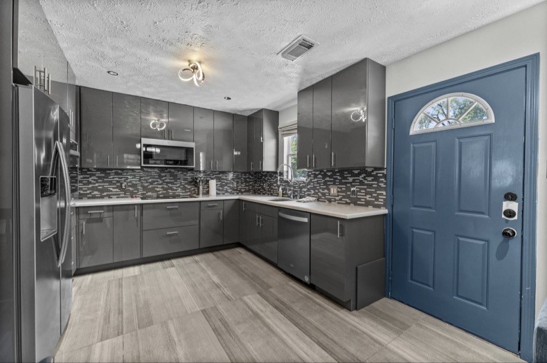 Guest-suite kitchen with wraparound counters, a tile backsplash, and an exterior entry door.