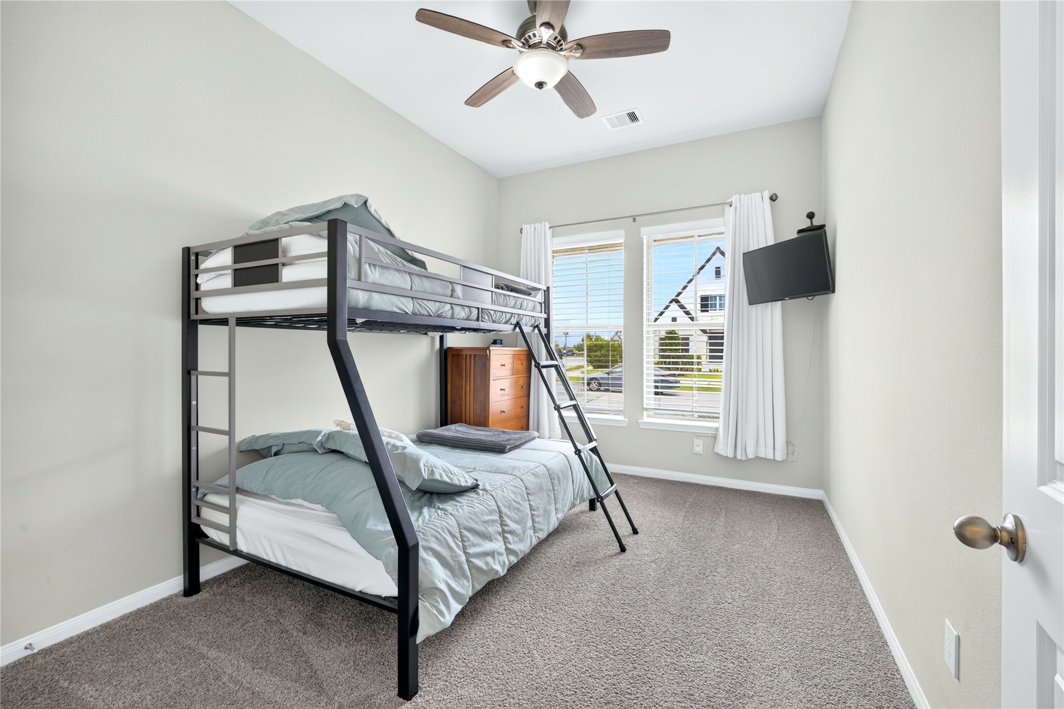 Front of the home bedroom featuring a large window, plush carpeting, ceiling fan, and a spacious walk-in closet. A bright and comfortable retreat with plenty of natural light and storage.