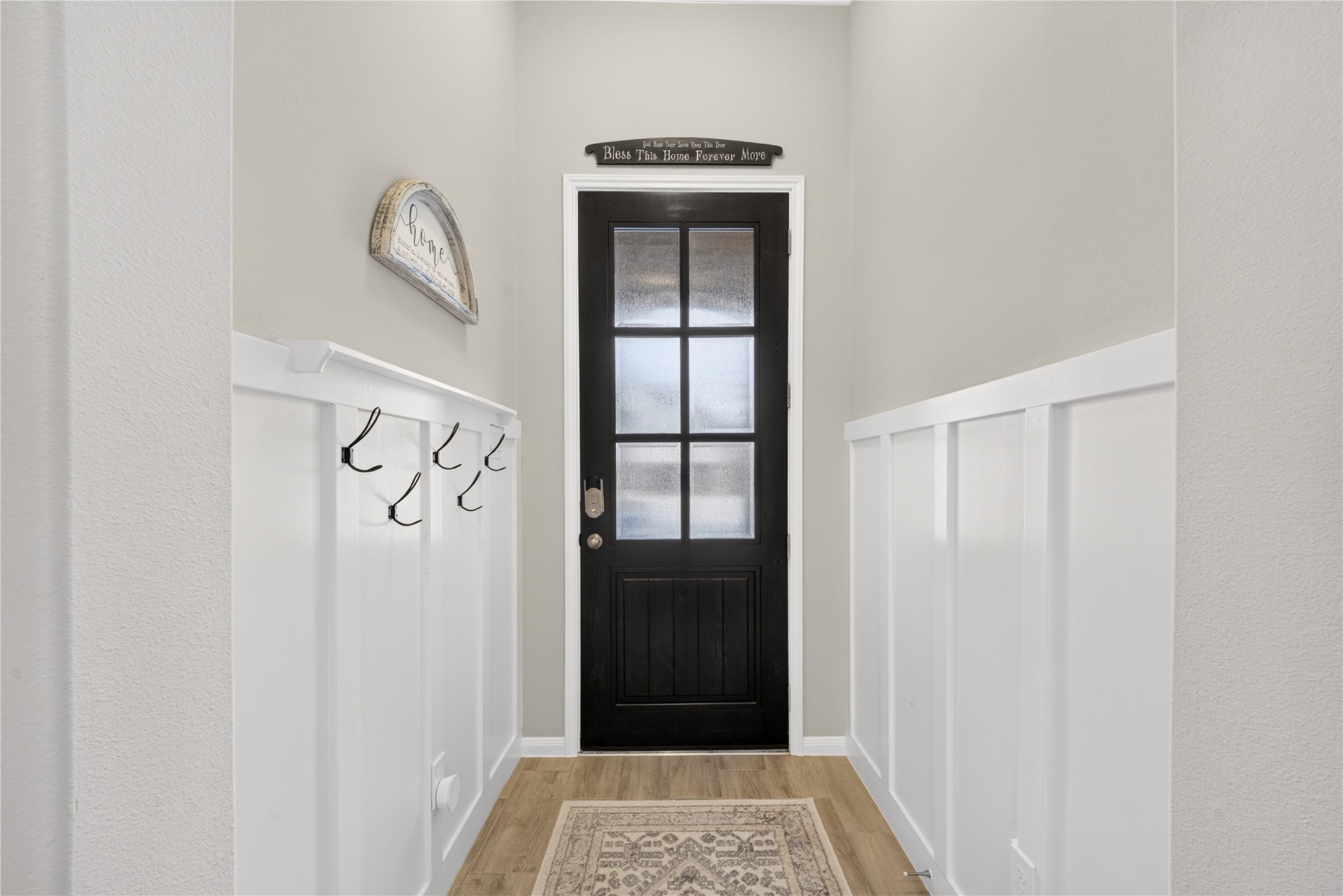 Welcoming hallway featuring beautiful white wainscoting, tile floors, stylish glass paneled front door. A convenient wall mounted hook area adds practical storage for coats, purses and every day essentials.