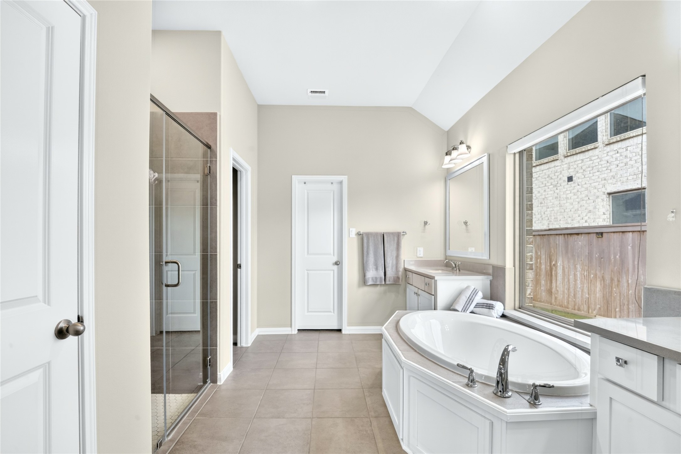 Clean and serene, the primary bathroom offers a spa-like retreat with dual sinks, designer mirrors, a walk-in shower, and elegant tile flooring.