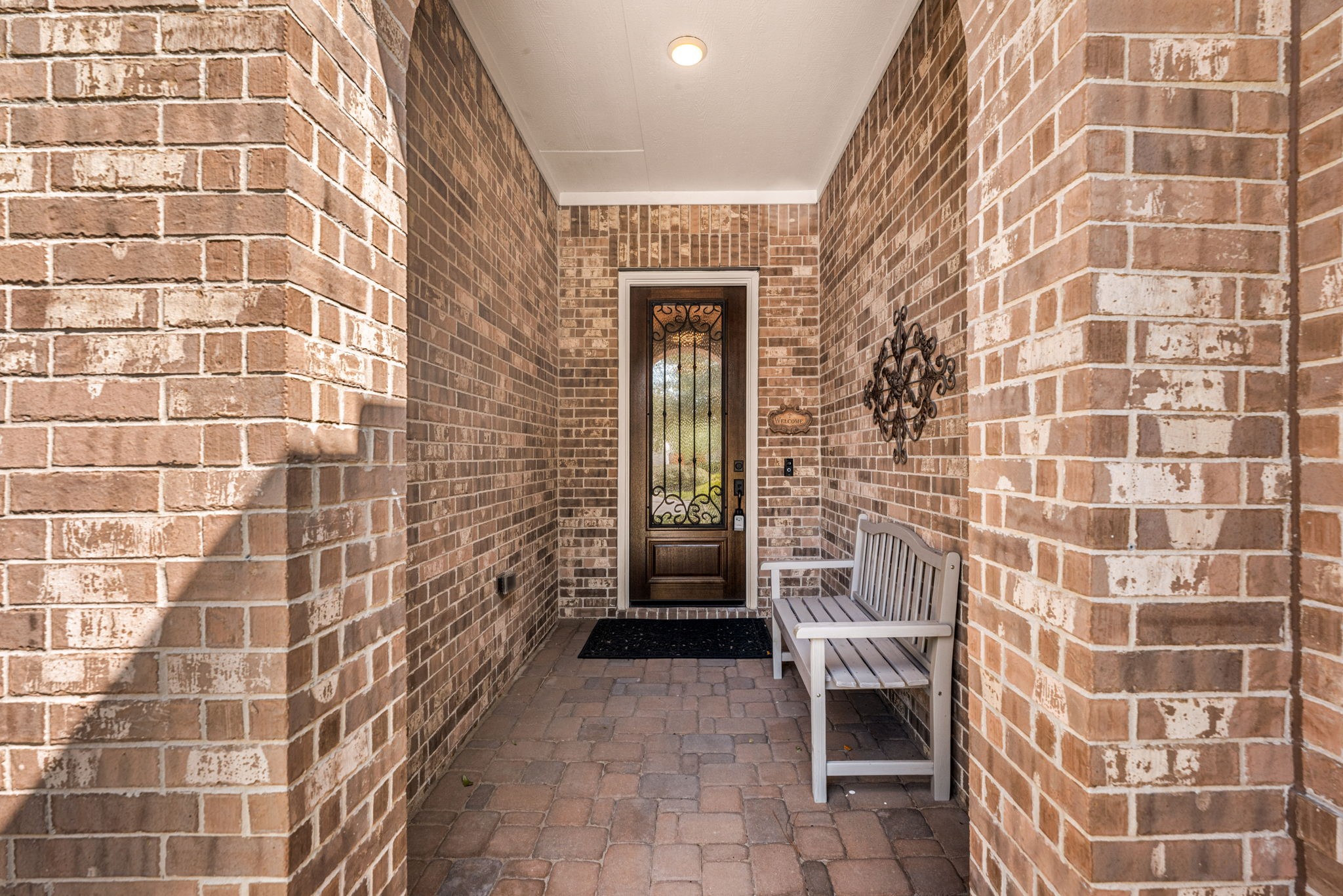 Step inside this charming covered entry featuring beautiful brickwork, a welcoming sitting area, and an elegant front door with decorative wrought iron detailing!