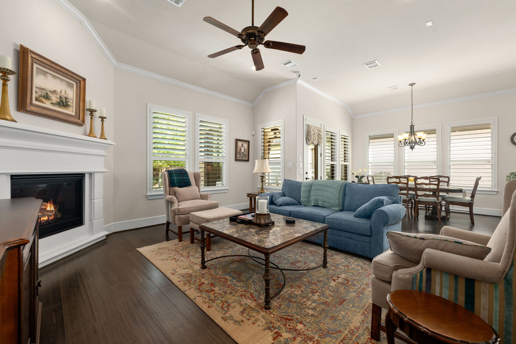 Relax and unwind in this spacious, light-filled living room featuring soaring ceilings, beautiful wood flooring, a cozy fireplace, and plantation shutters.