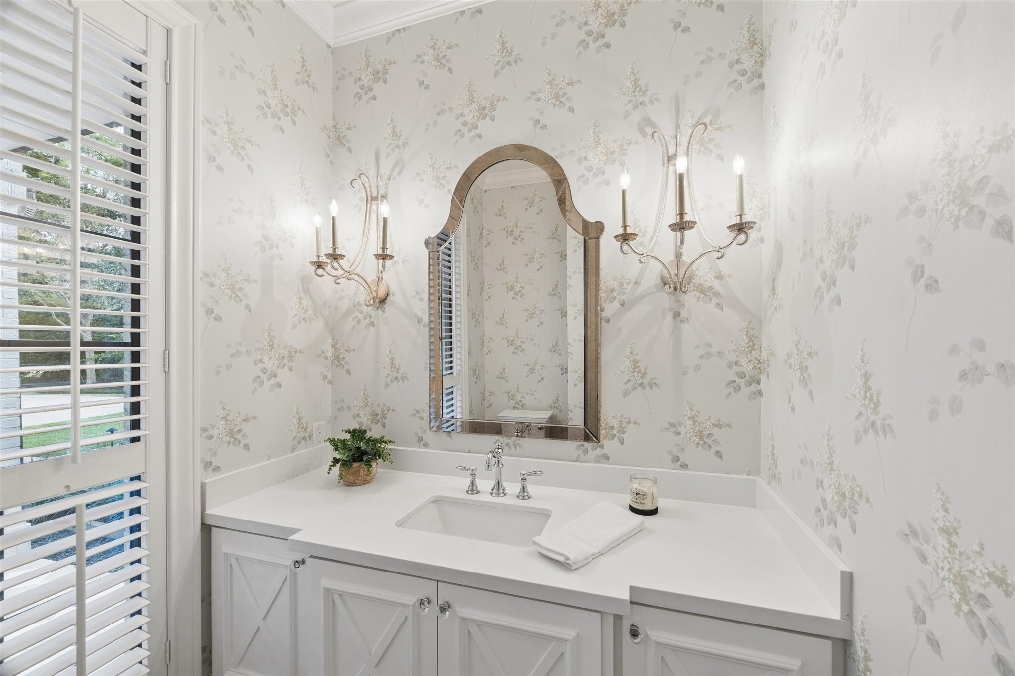 Elegant bathroom with floral wallpaper, featuring a classic vanity, arched mirror, and stylish wall sconces for a touch of sophistication.
