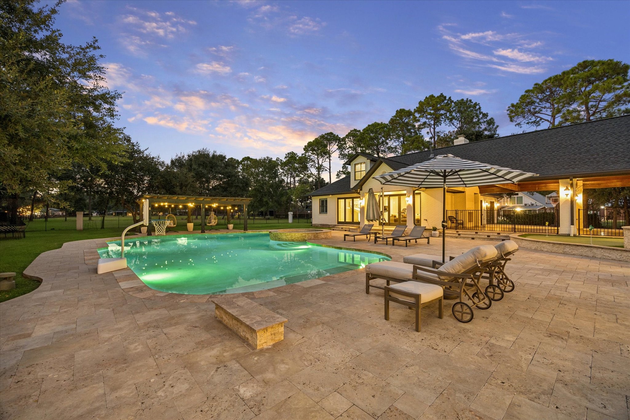 View of the backyard from the outdoor kitchen, featuring the pool house, porte-cochre, and putting green in the background.