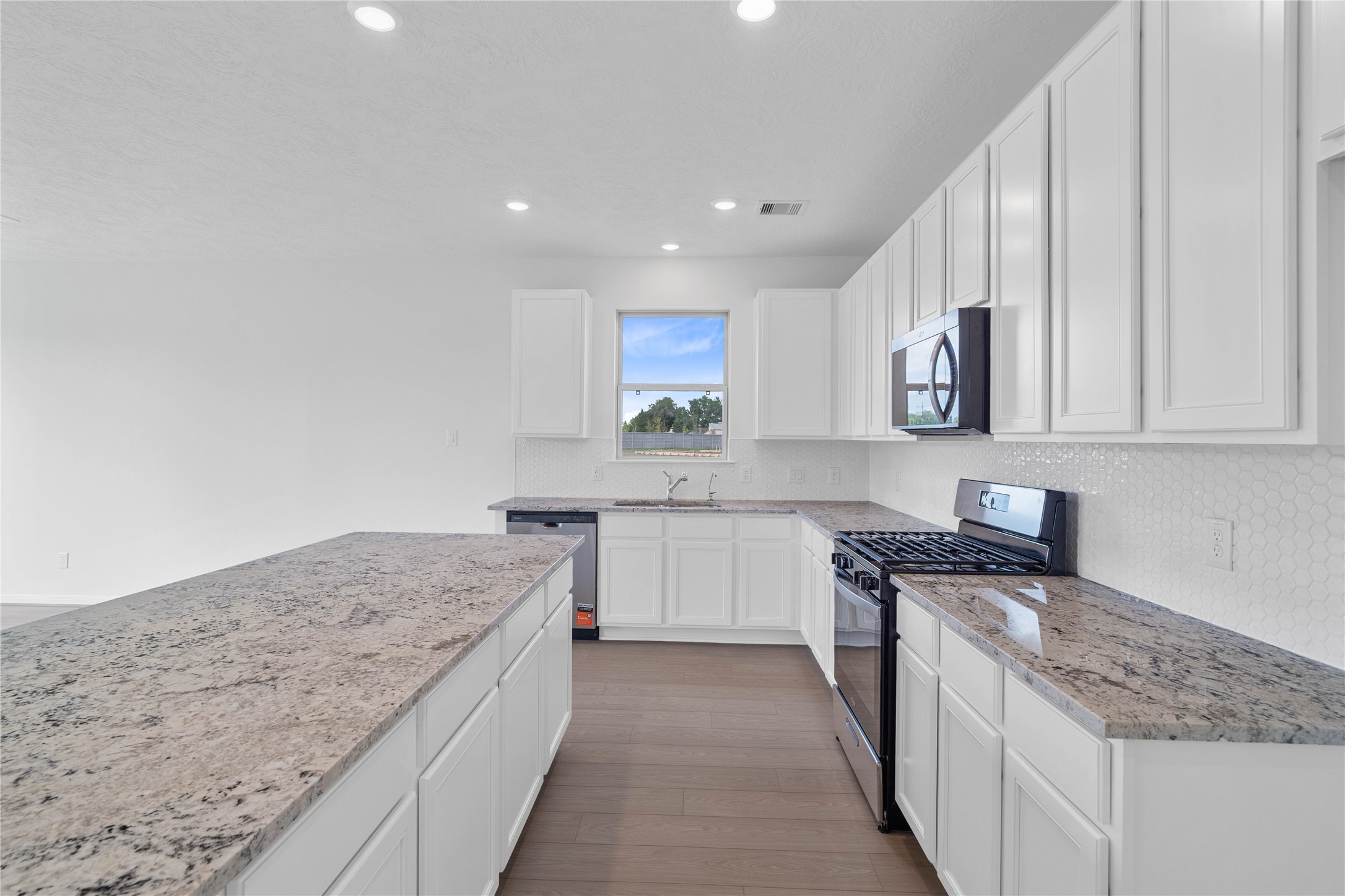 This spacious kitchen features high ceilings, white Woodmont Belmont cabinets, granite countertops in White Ice, Whirlpool stainless steel appliances, Daltile tile backsplash, recessed lighting, and a pantry all overlooking your huge family room.