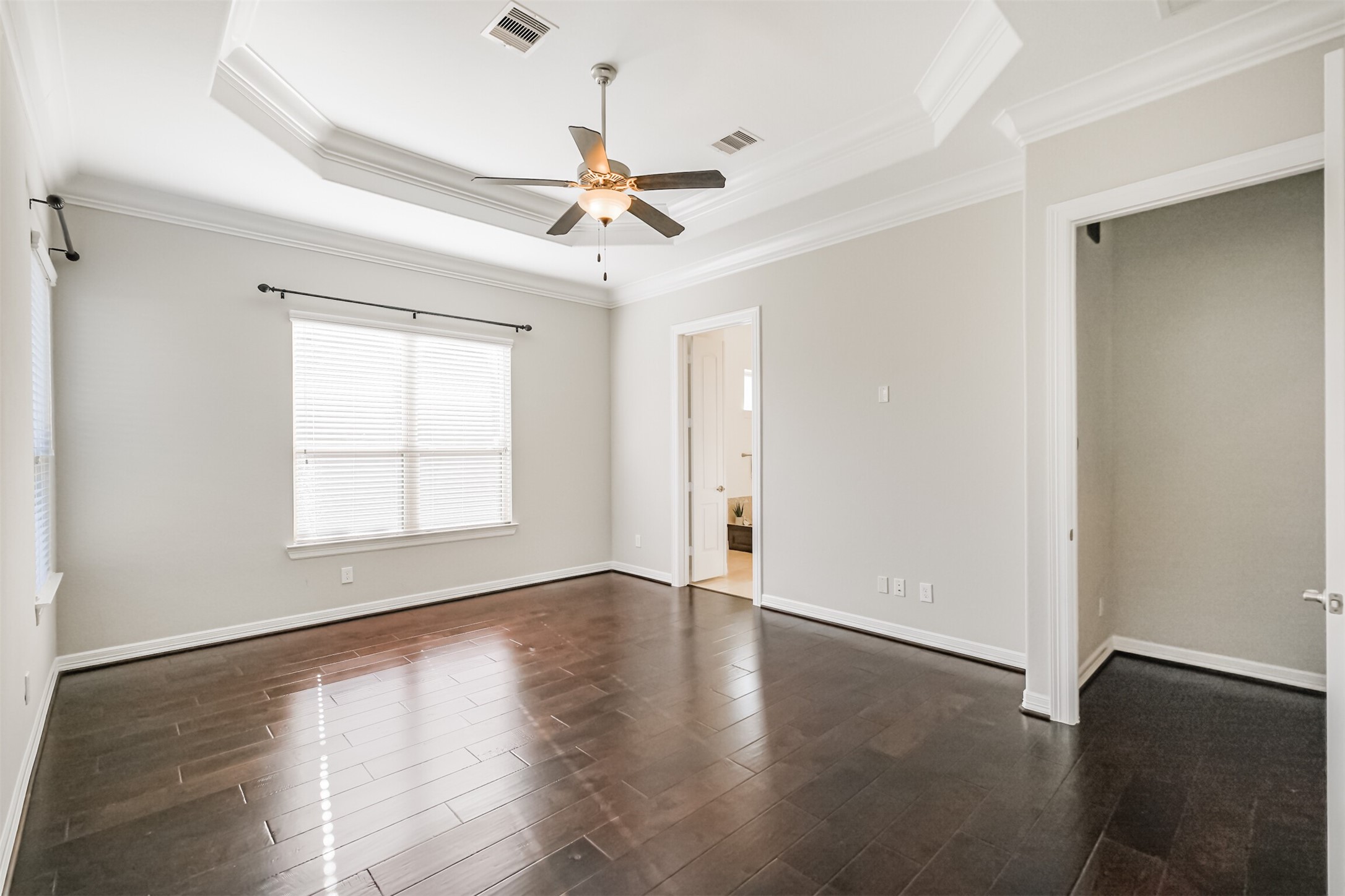 Spacious primary retreat featuring an elegant tray ceiling, crown molding and ceiling fan